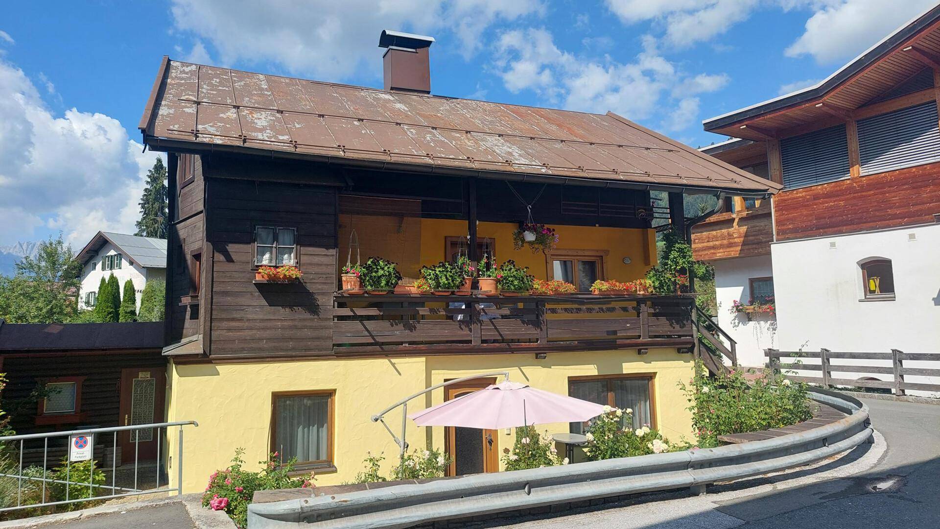 Charmantes altes Holzhaus mit blühendem Balkon und gelbem Anstrich in sonniger Lage.