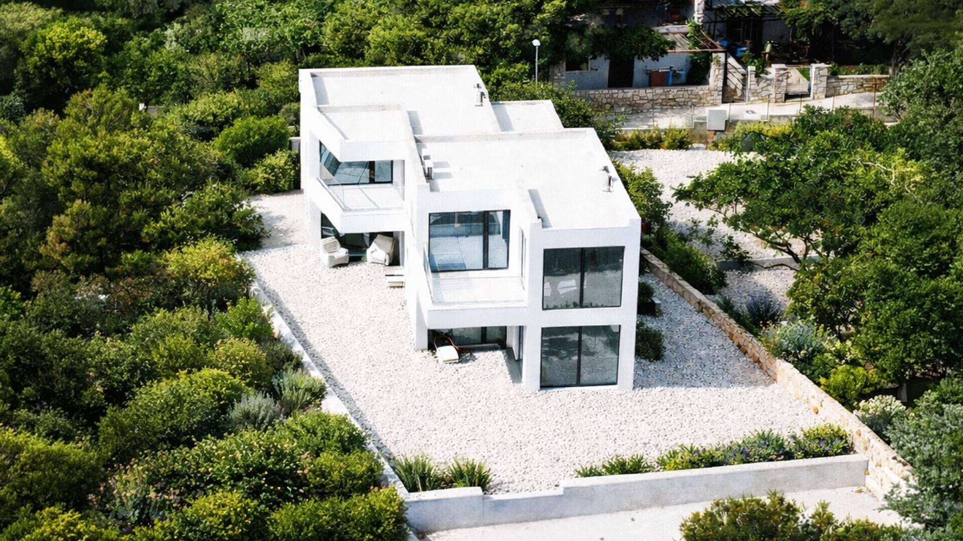 Luftaufnahme einer modernen Villa mit Flachdach, umgeben von üppiger grüner Vegetation.