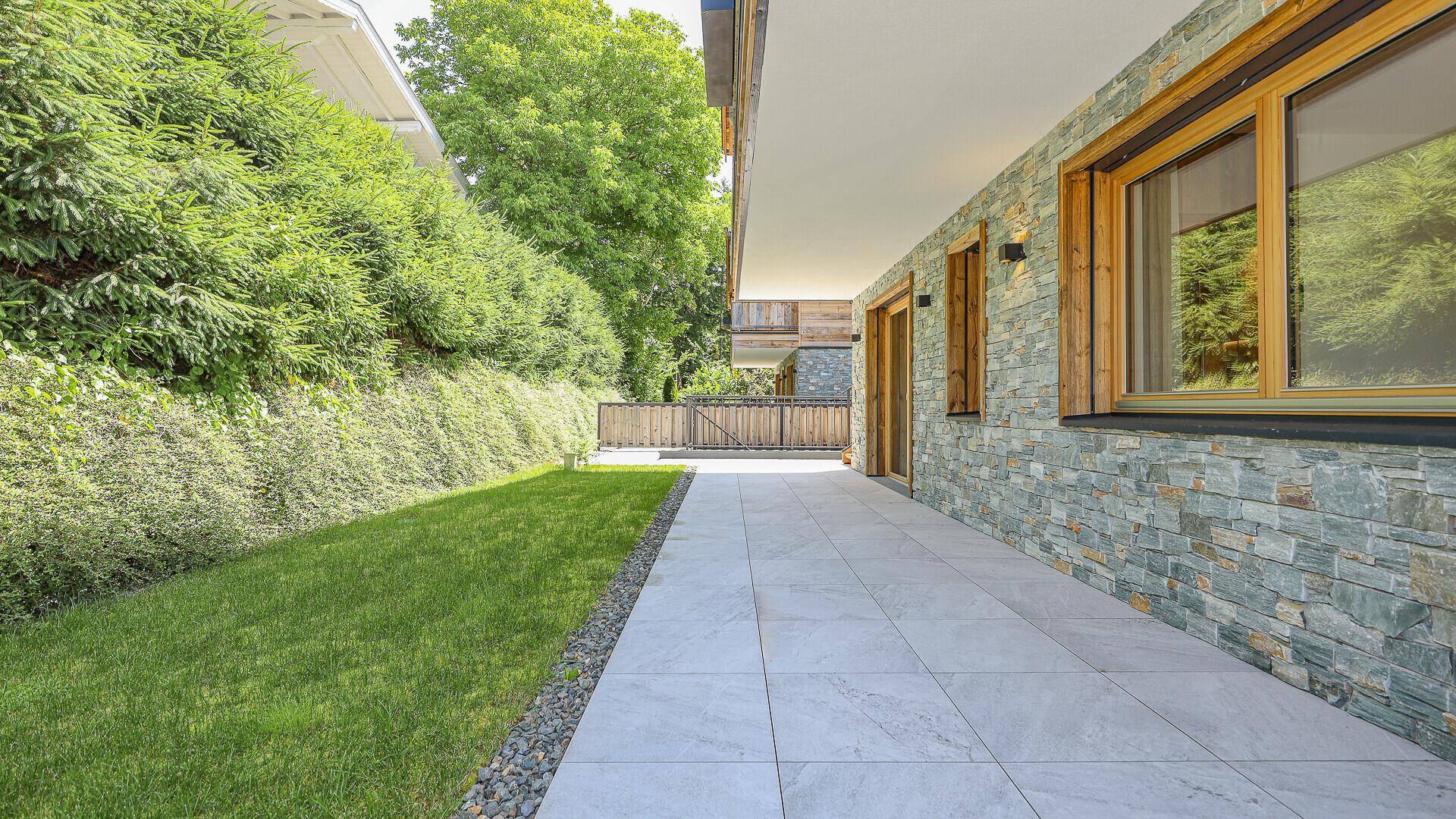 Seitlicher Gartenbereich mit Rasen, gepflastertem Weg und grüner Hecke.