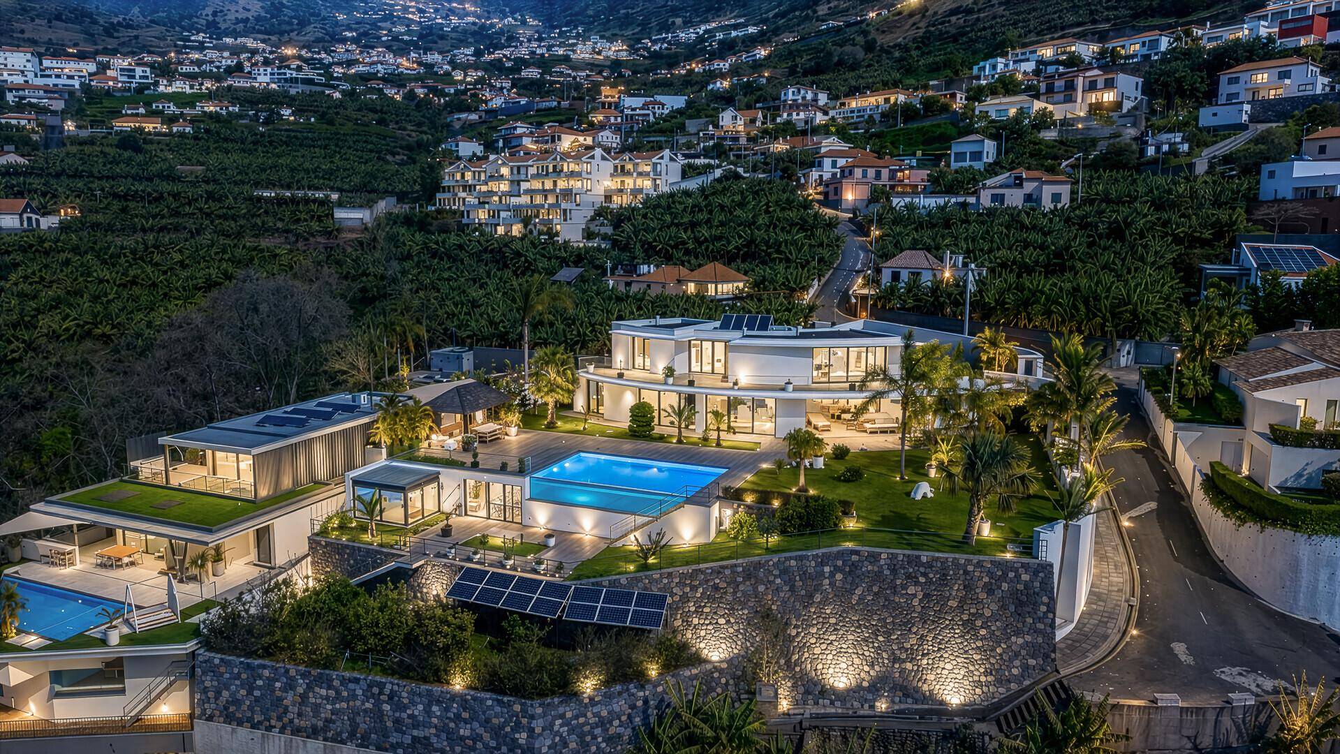 Luxuriöse Villa bei Nacht, umgeben von beleuchteten Gärten und Bananenplantagen mit Blick auf die Stadt.