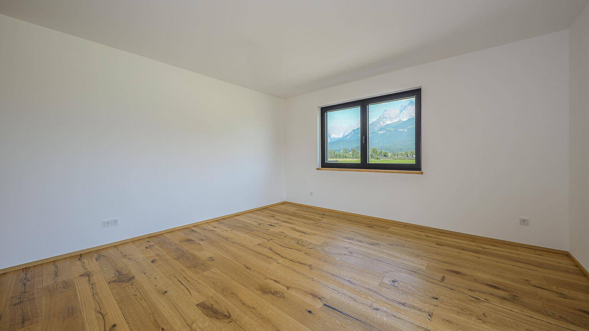 Leerer Raum mit Holzboden und großem Fenster, das einen weiten Bergblick bietet.