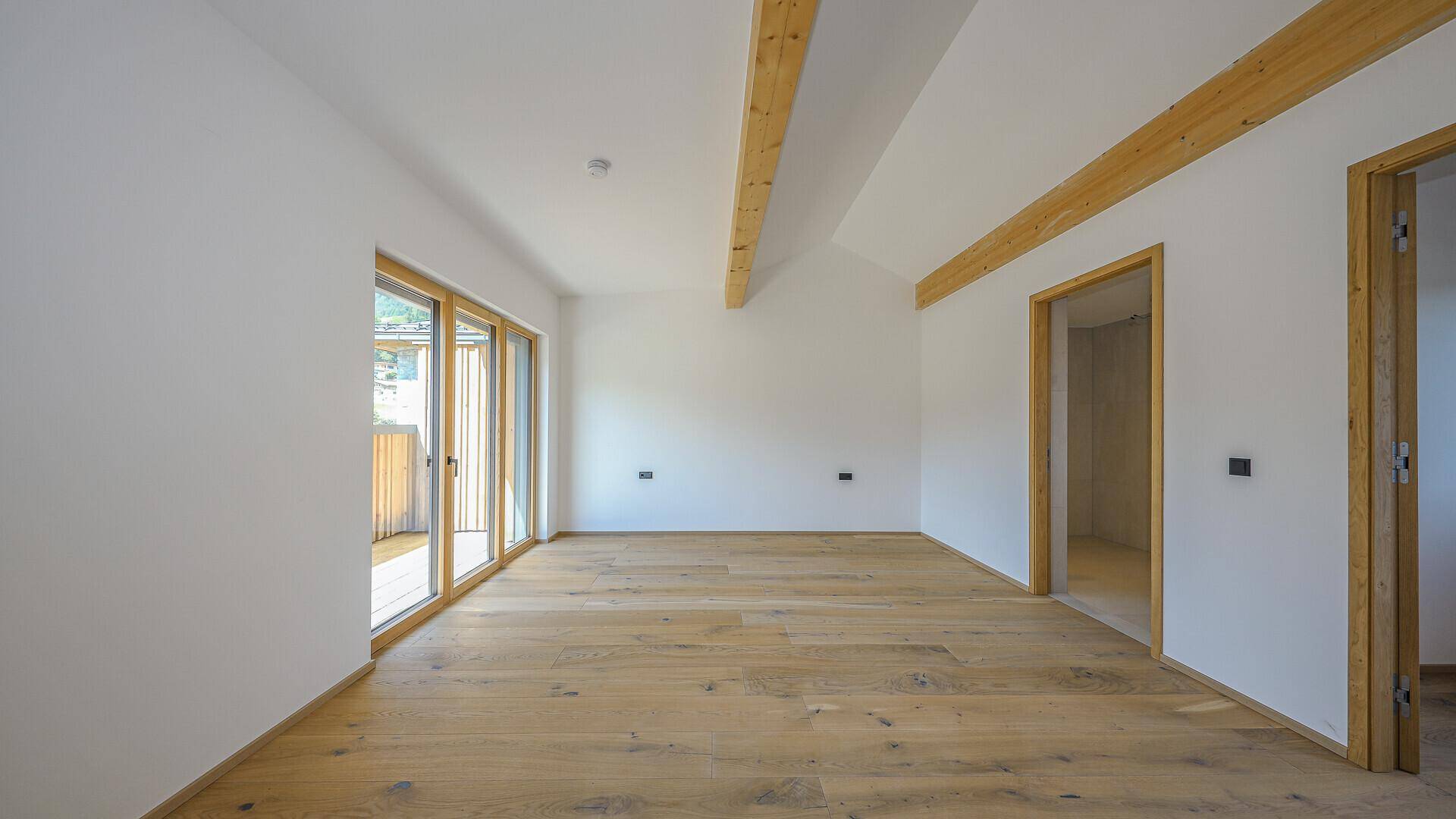 Heller Raum mit Holzboden, Dachschräge und Zugang zu einem Balkon, ideal als Schlafzimmer.