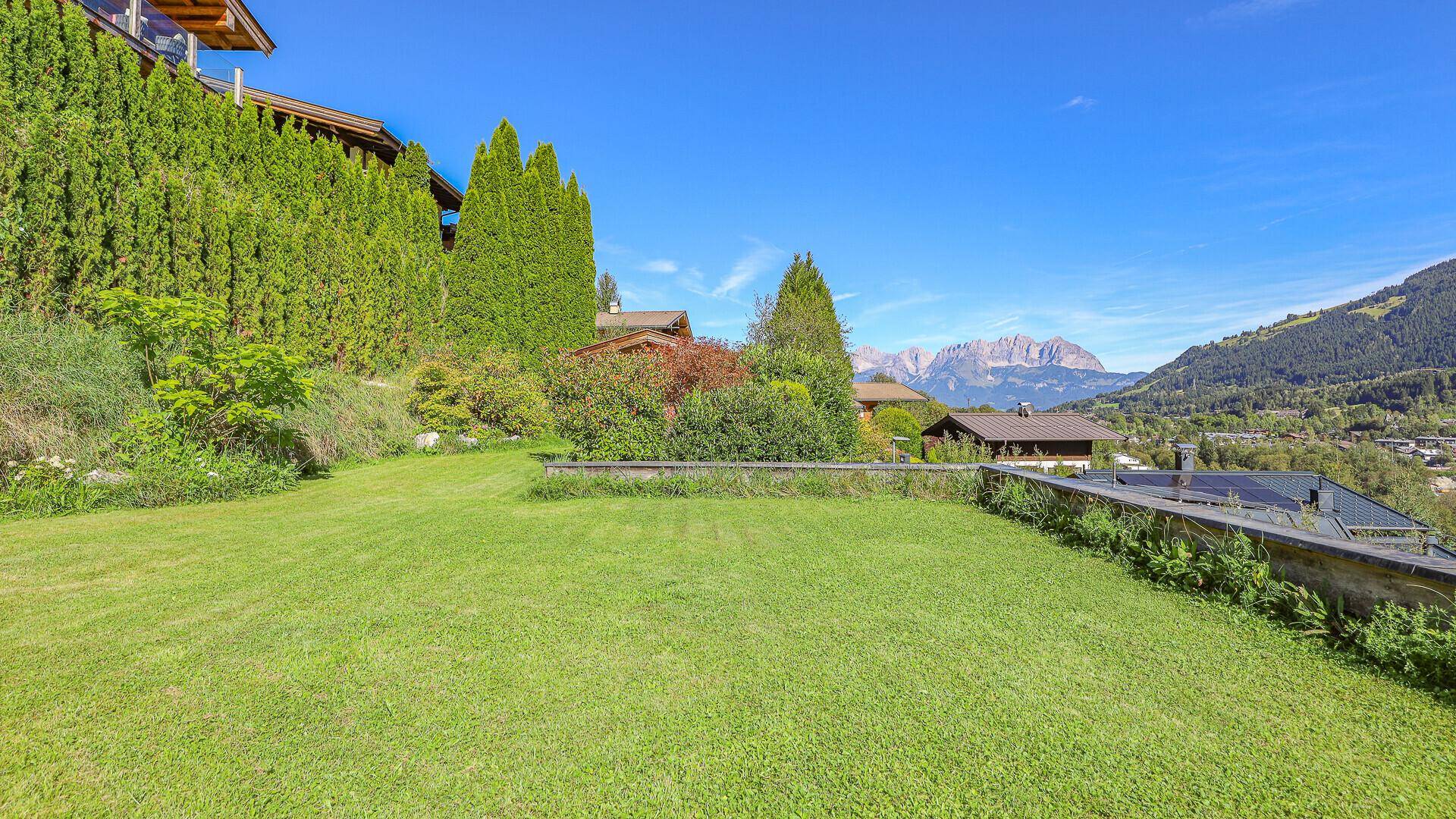 Große Rasenfläche im Garten mit weitem Blick auf die majestätische Bergkette und die grüne Umgebung.