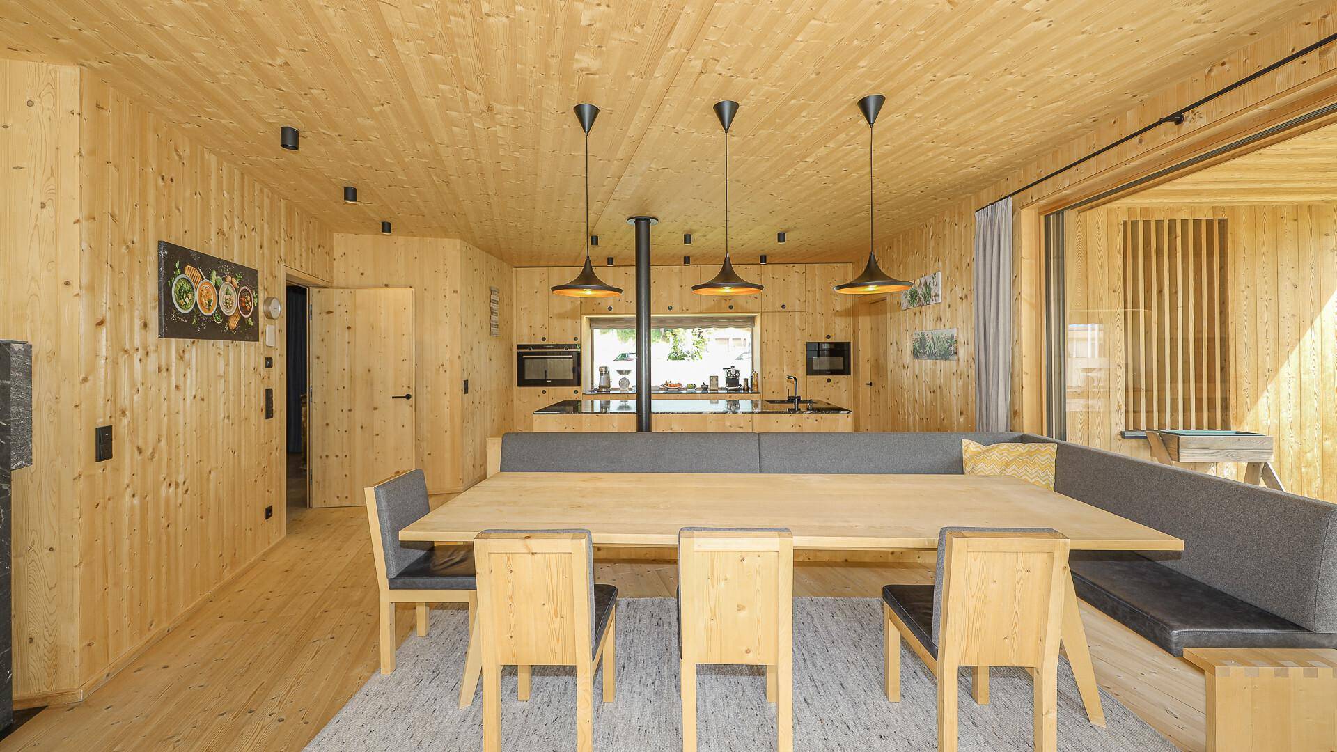 Heller Essbereich mit Holztisch und integrierter Sitzbank, offener Küche und Holzwänden.