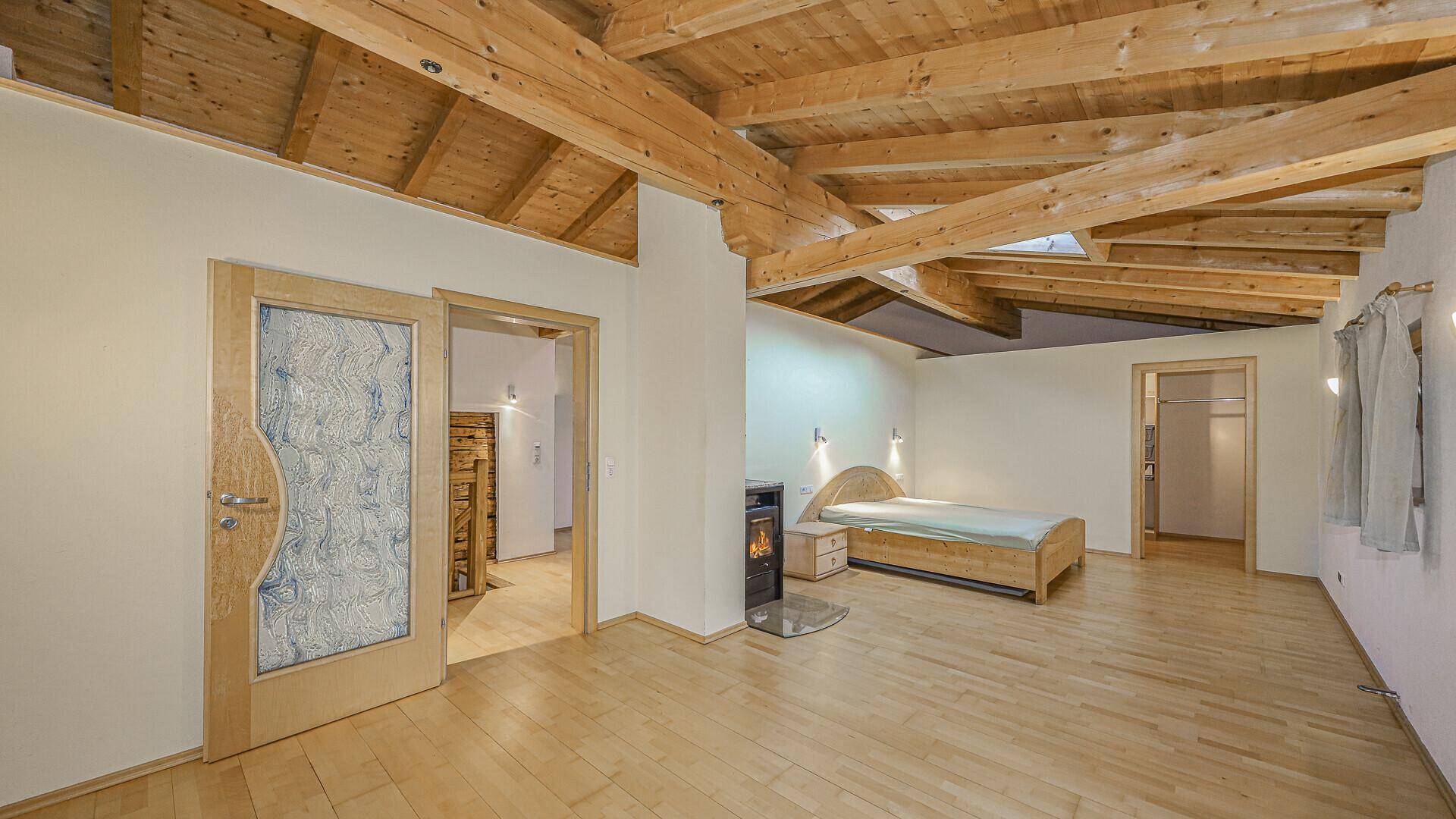 Helles Schlafzimmer mit Holzbalkendecke, Dachfenstern und Kaminofen, bietet viel Gemütlichkeit.