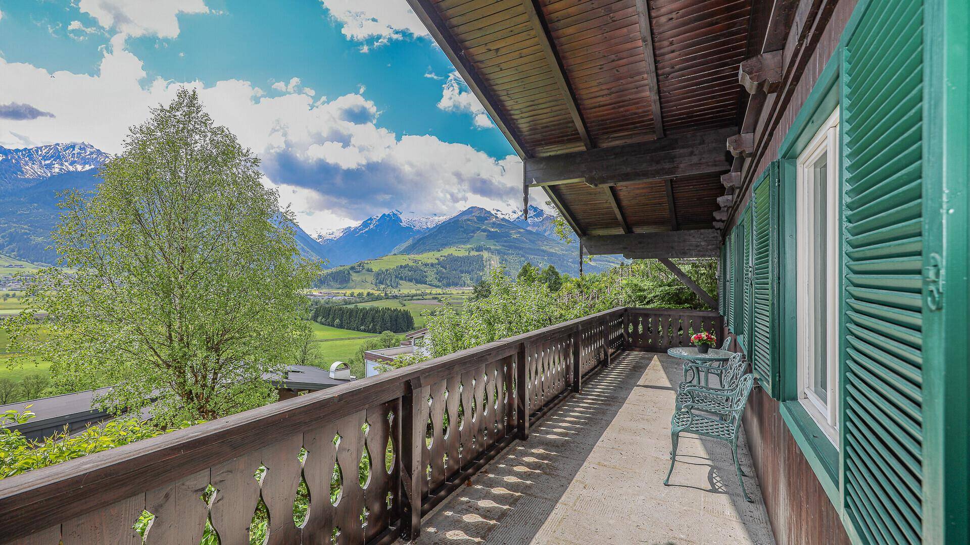Überdachter Balkon mit Sitzgelegenheiten und Panoramablick auf die Alpen und grüne Landschaft.