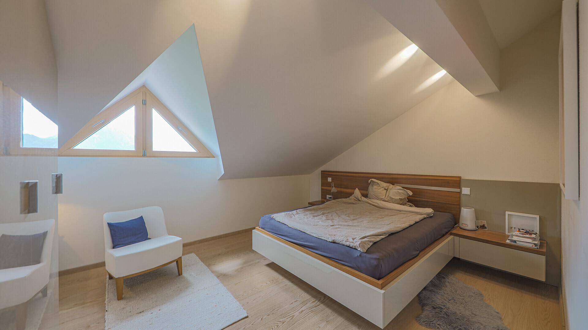 Helles Schlafzimmer im Dachgeschoss mit schrägen Wänden, modernen Möbeln und einzigartigen dreieckigen Fenstern.