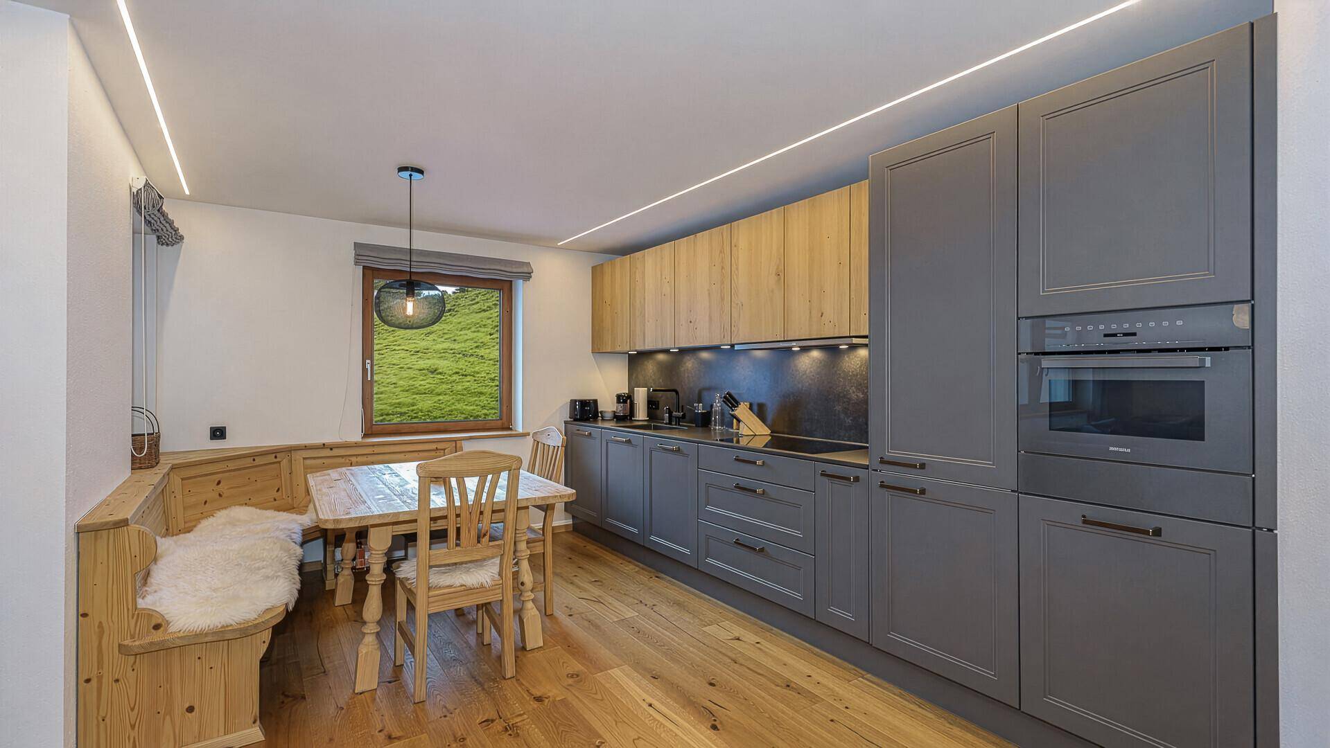 Moderne Küche mit grauen und holzfarbenen Schränken, Essbereich und Blick ins Grüne.