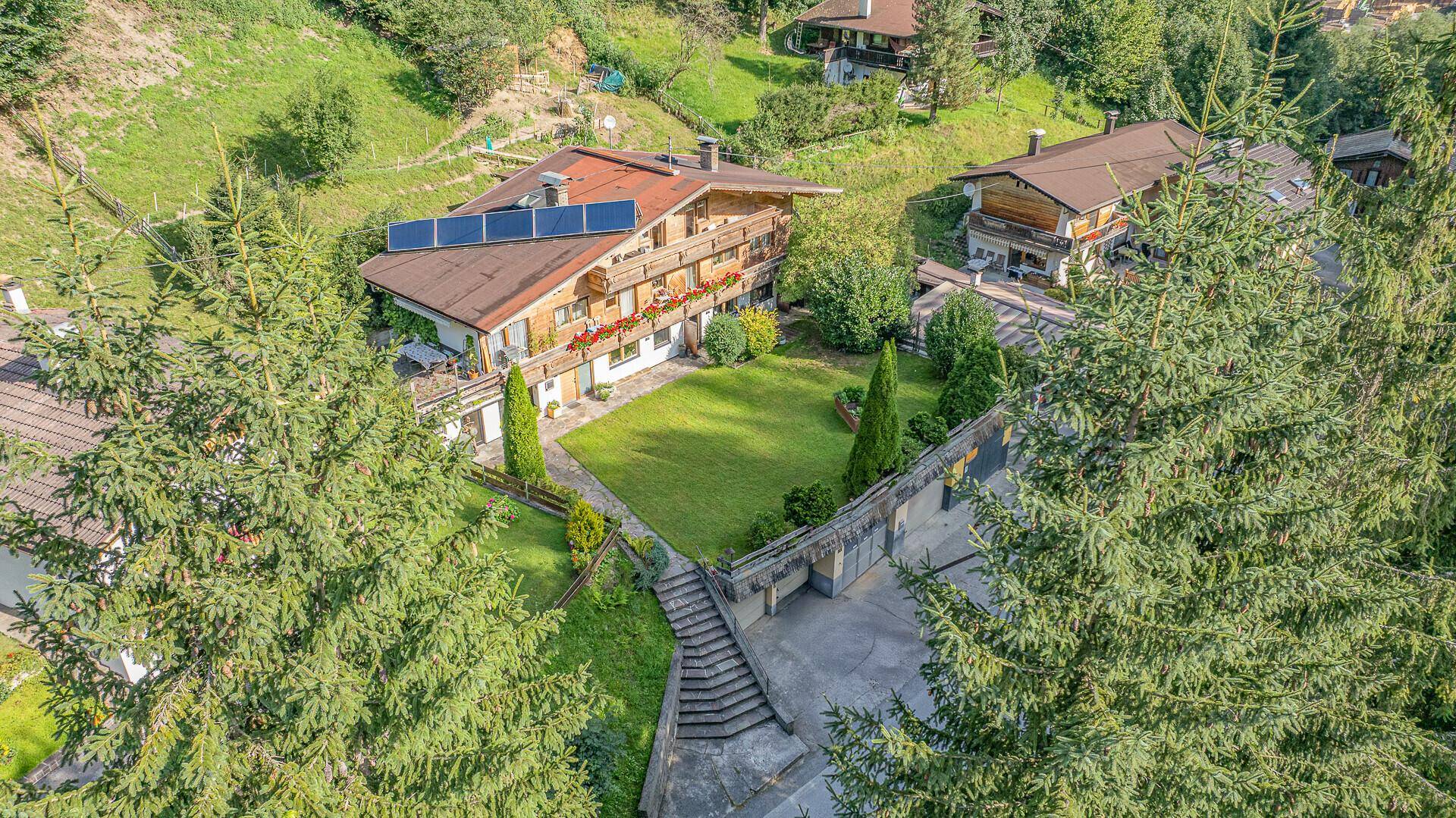 Luftaufnahme eines Chalets mit Photovoltaikanlage, Garten und umliegender Berglandschaft.