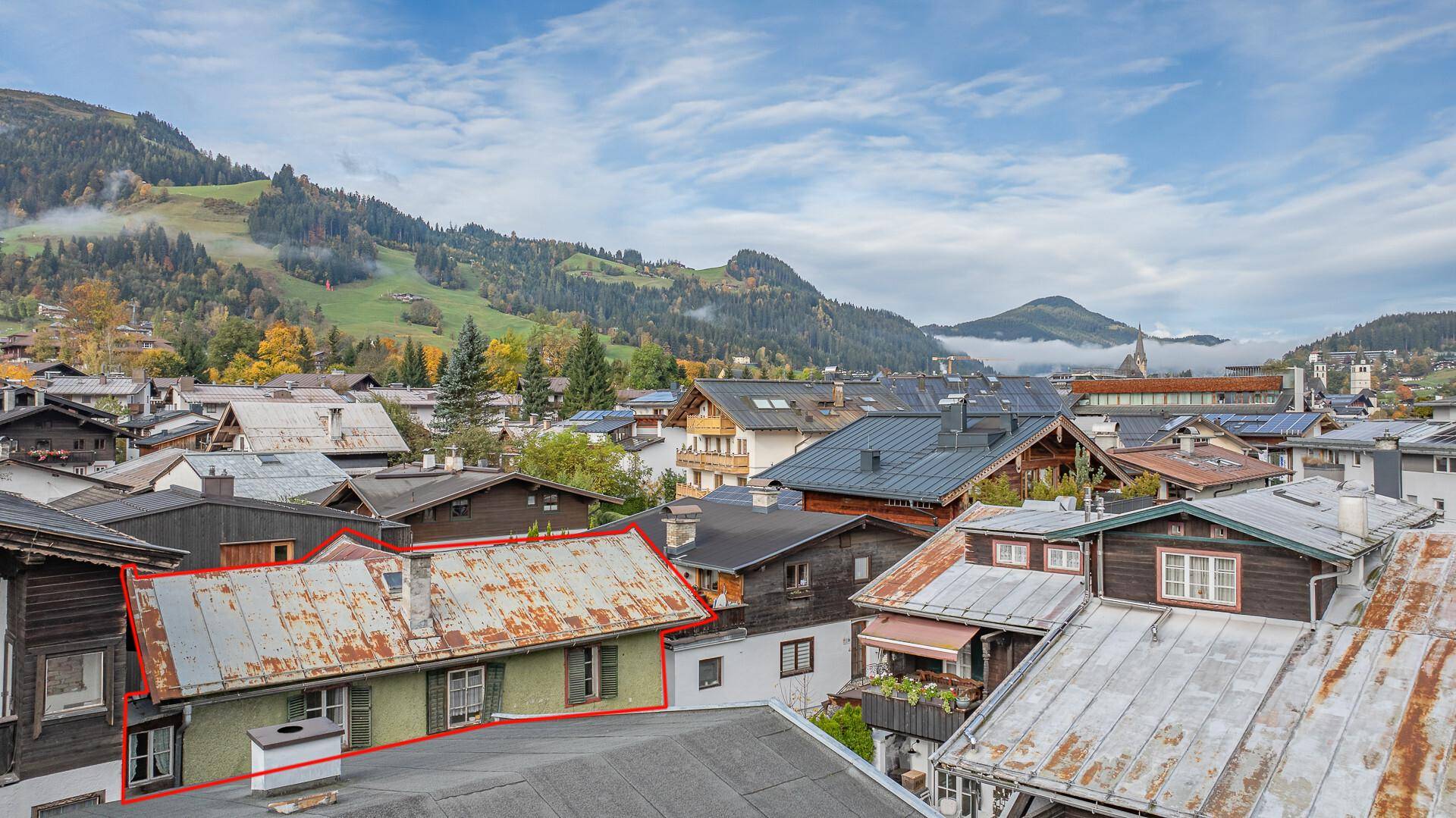 Luftaufnahme eines älteren Hauses mit grünlicher Fassade und Bergblick in einer Siedlung.