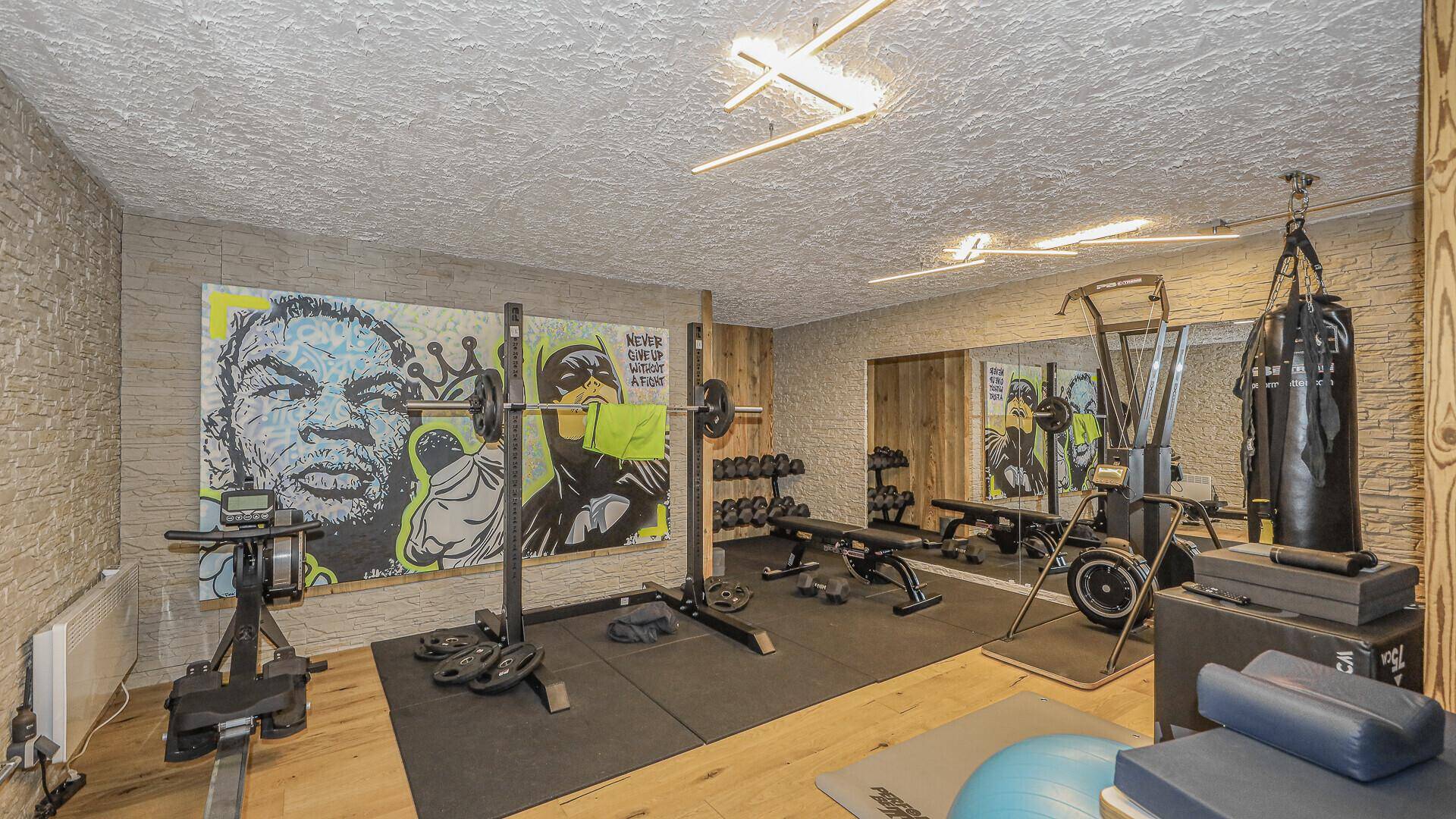 Gut ausgestatteter Fitnessraum mit verschiedenen Trainingsgeräten, Boxsack und auffälliger Wandmalerei.
