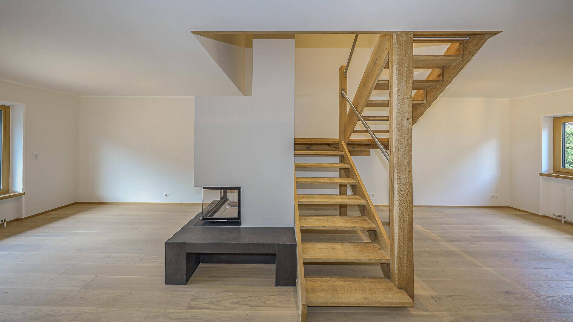 Geräumiger, unmöblierter Raum mit hellem Holzboden, Kamin und markanter Holztreppe.