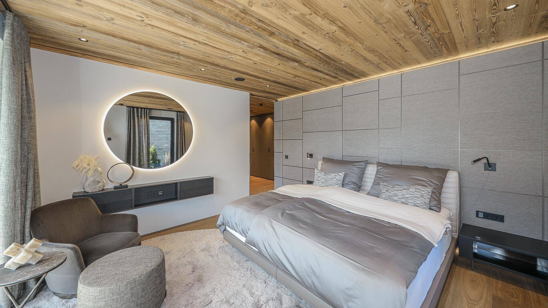 Stilvolles Schlafzimmer mit Holzbalkendecke, runder Spiegelleuchte und modernen Wandpaneelen.