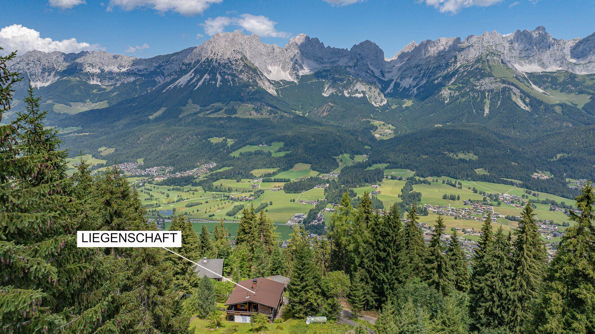 Weitläufiger Blick auf die Liegenschaft, eingebettet in Wälder mit einem Tal und Bergen im Hintergrund.