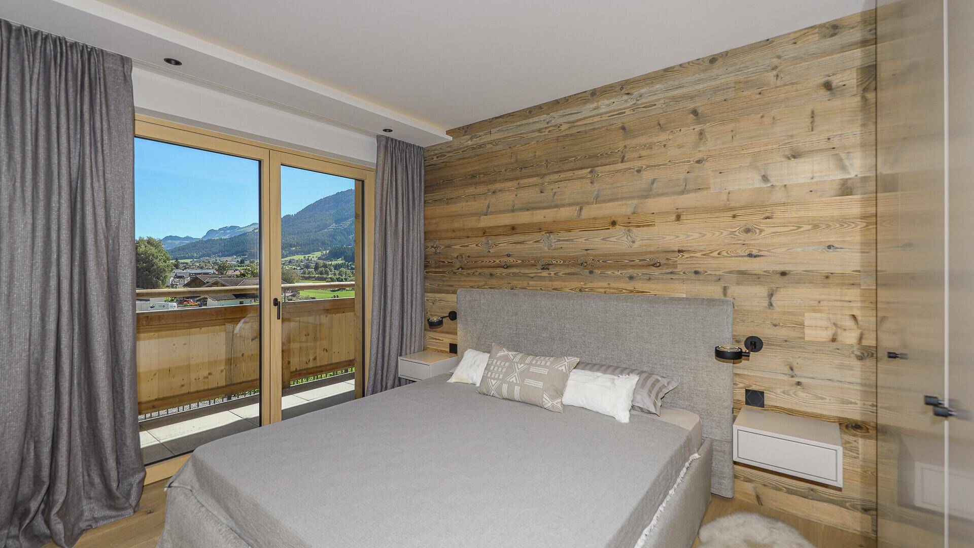 Gemütliches Schlafzimmer mit Holzwand, Doppelbett und Zugang zum Balkon mit Bergblick.