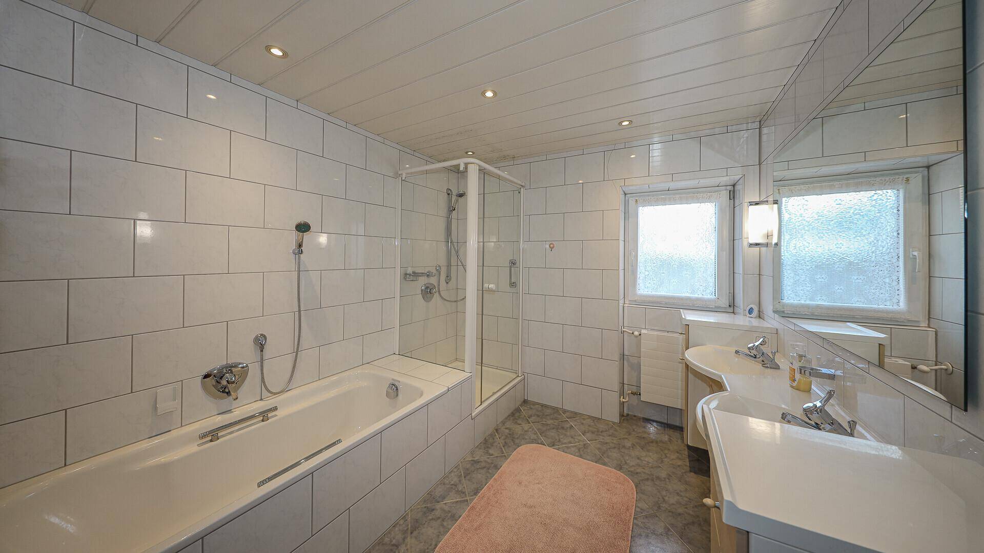 Geräumiges Badezimmer mit Badewanne, Dusche, Doppelwaschbecken und Fenster.