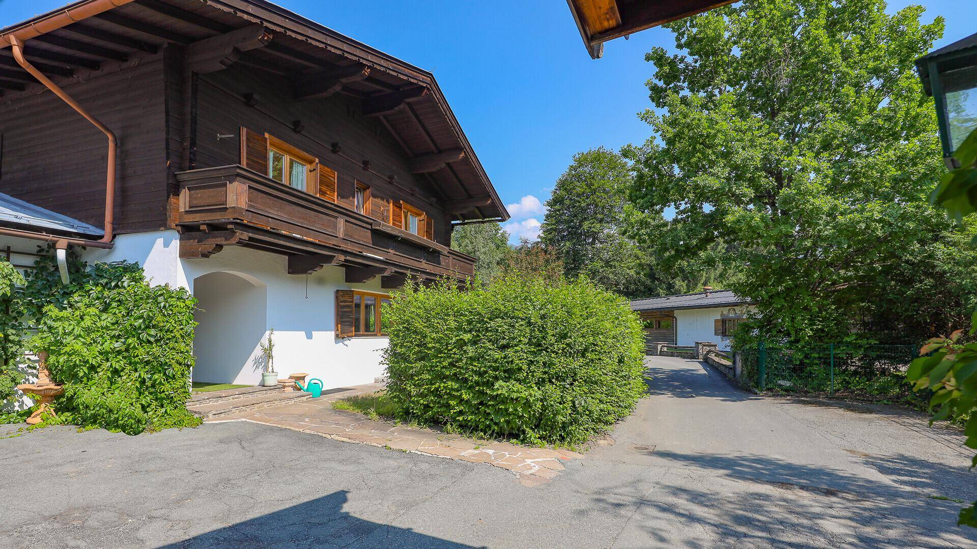 Zufahrt zum traditionellen Chalet, umgeben von üppiger Vegetation und Hecken.