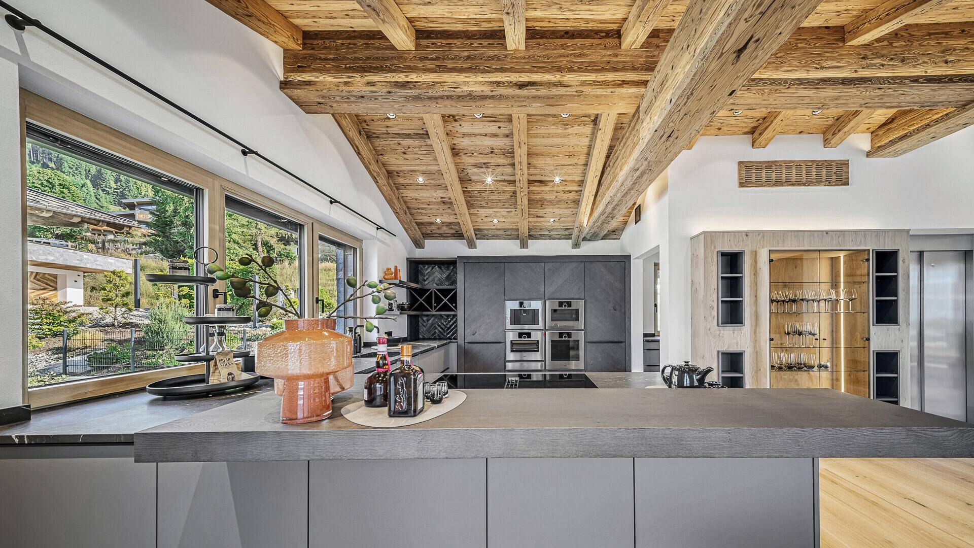 Moderne Küche mit Kücheninsel, dunklen Schränken und großem Fenster mit Blick ins Grüne.