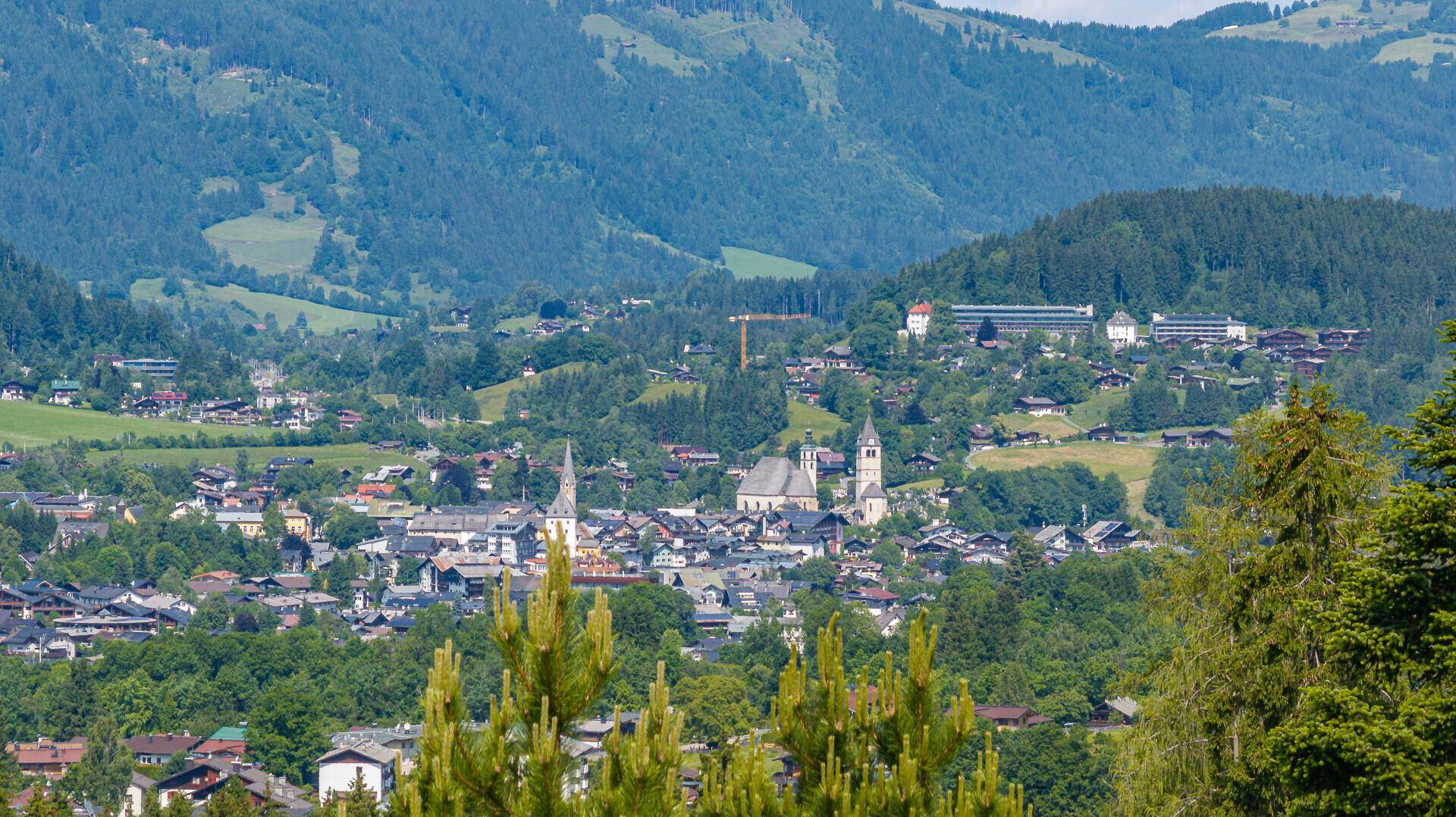 Weitläufiger Blick auf ein malerisches Dorf im Tal, umgeben von grünen Hügeln und Bergen.