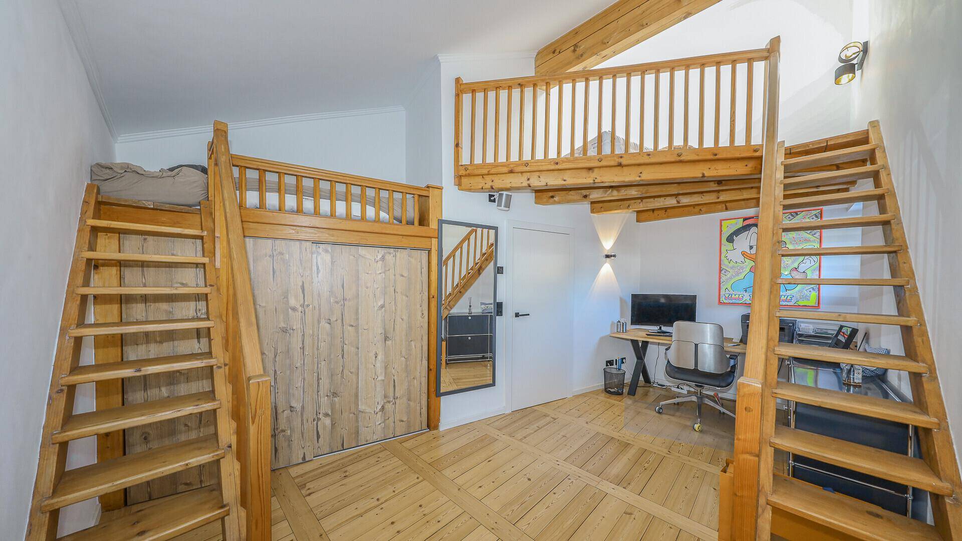 Kreativ gestaltetes Kinder- oder Gästezimmer mit Hochbetten und einem Arbeitsbereich unter freiliegenden Holzbalken.