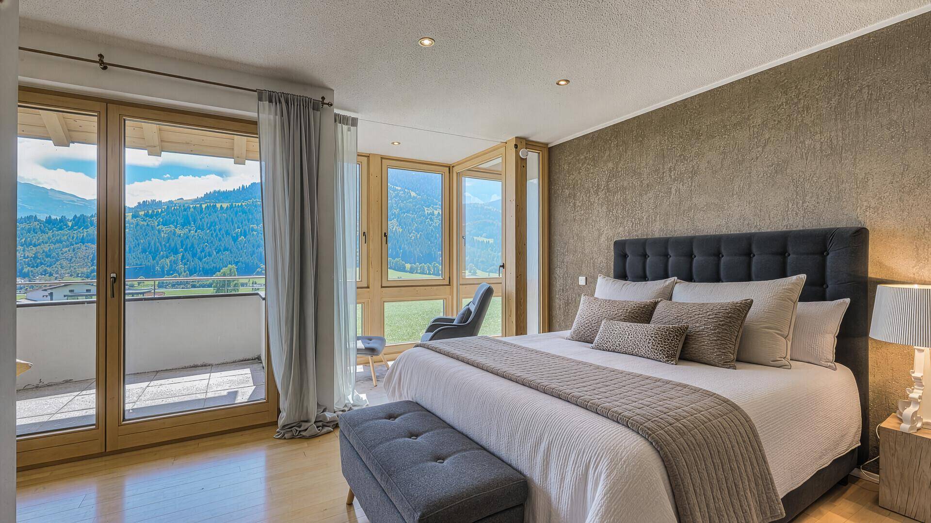Helles Schlafzimmer mit Doppelbett, Balkonzugang und atemberaubendem Blick auf die Berge.