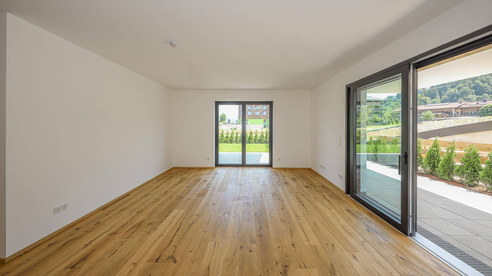 Heller Wohnraum mit Holzboden und Schiebetüren, die auf eine Außenterrasse führen.