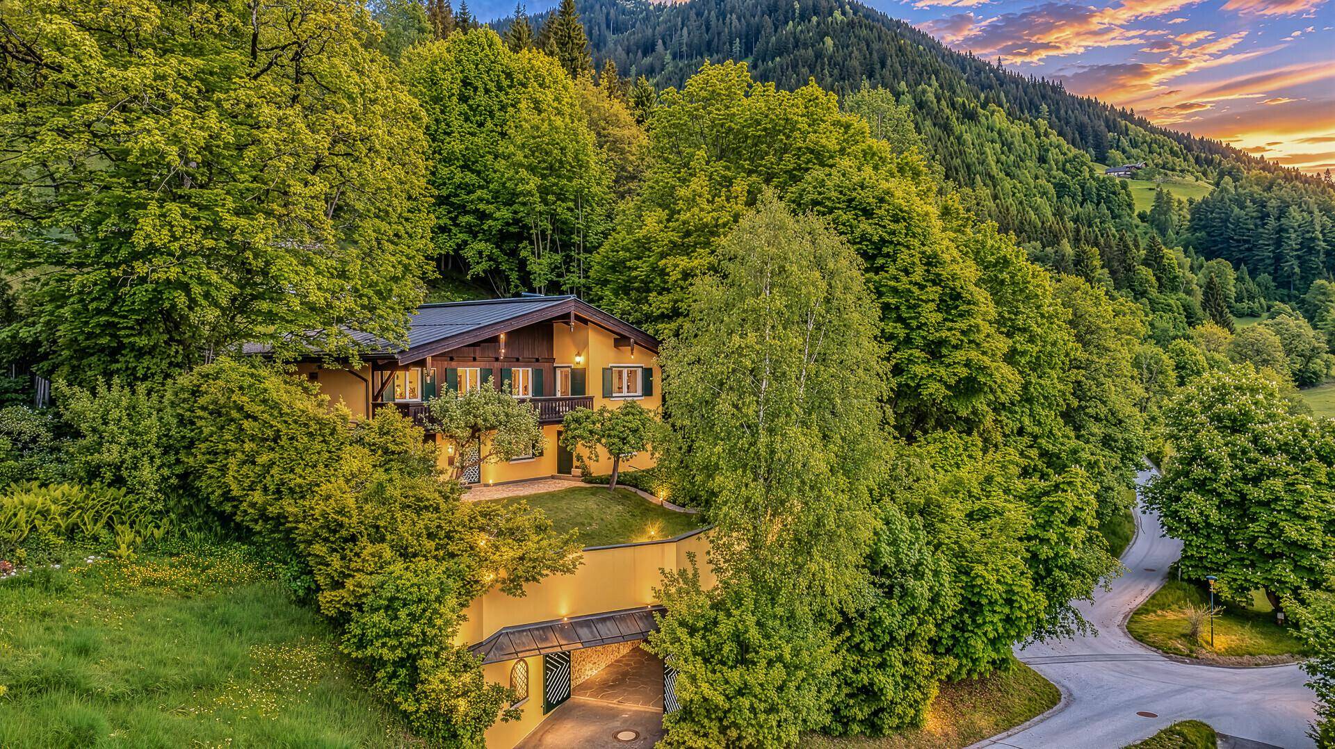 Luftaufnahme des Hauses mit gelber Fassade, umgeben von üppiger grüner Landschaft und Bergen bei Sonnenuntergang.