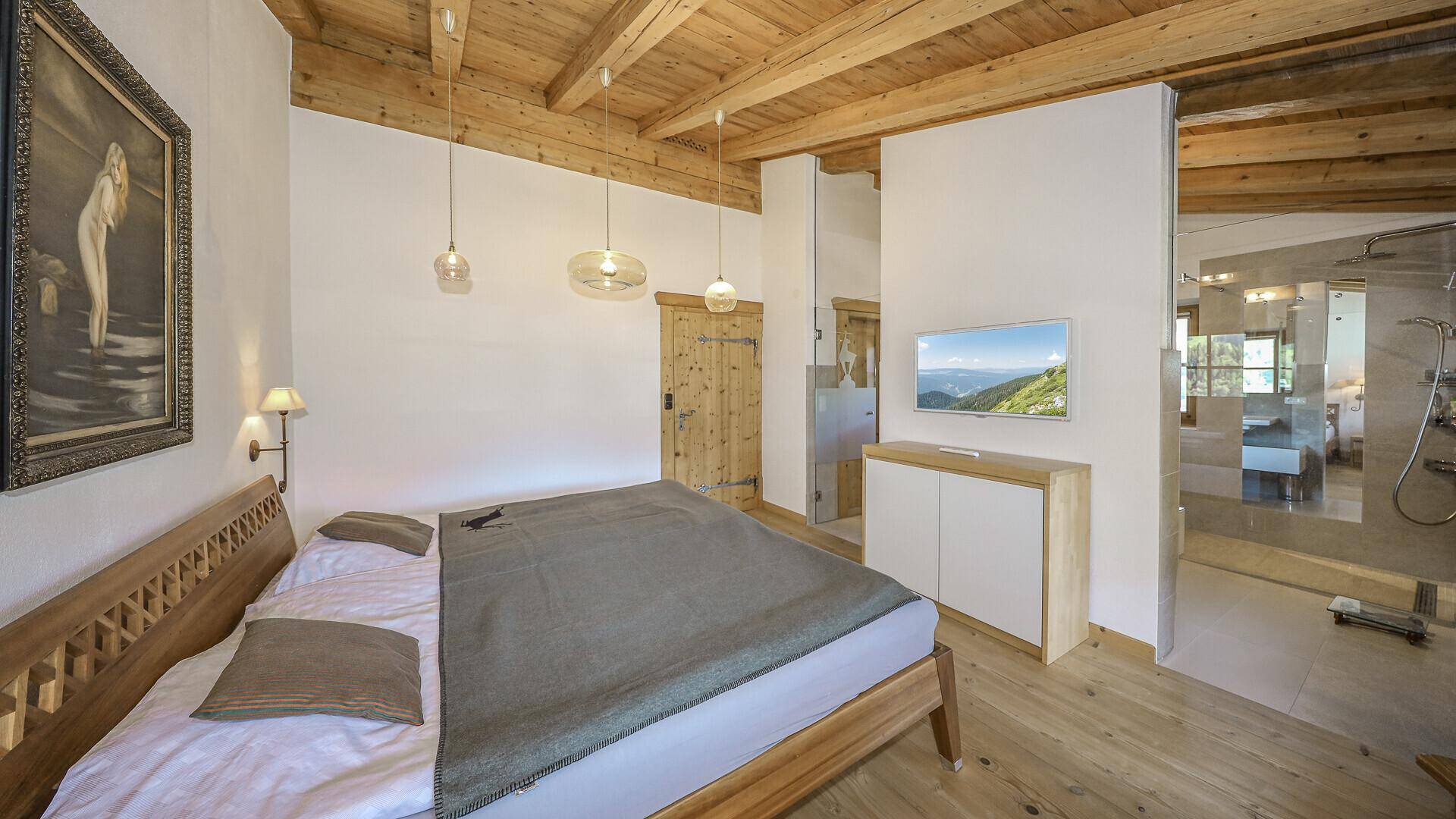 Helles Schlafzimmer mit Holzbalkendecke, Holzboden und offenem Zugang zum Badezimmer.