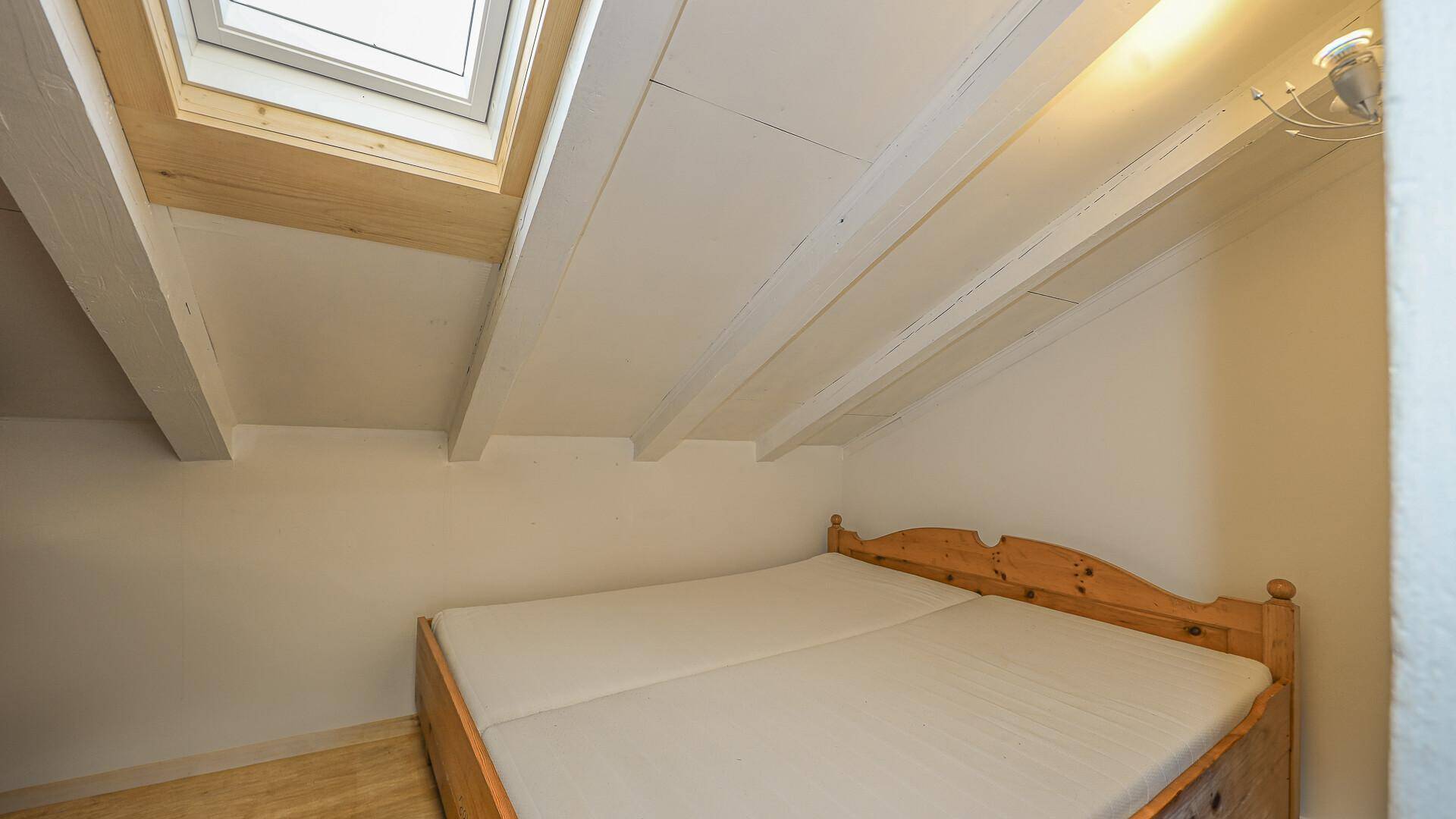Kleines Schlafzimmer im Dachgeschoss mit Holzbett, Dachfenster und schrägen Wänden.