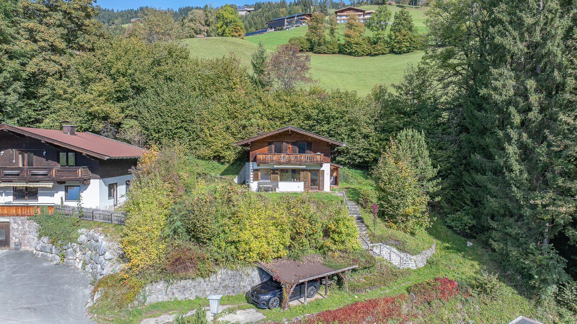 Traditionelles Holzhaus mit Carport und Treppe, eingebettet in eine grüne Hügellandschaft.