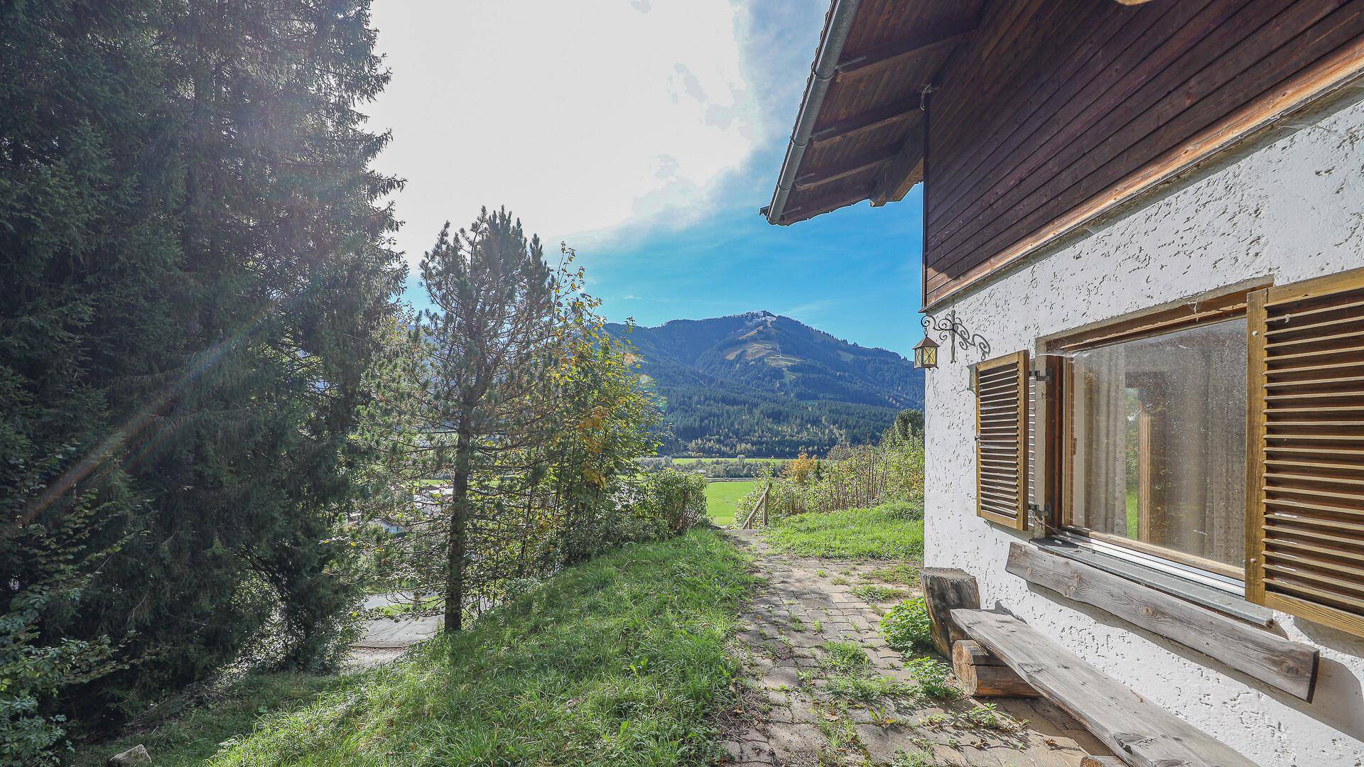 Gartenweg neben dem Haus mit Blick auf die Berge und grüne Natur unter blauem Himmel.
