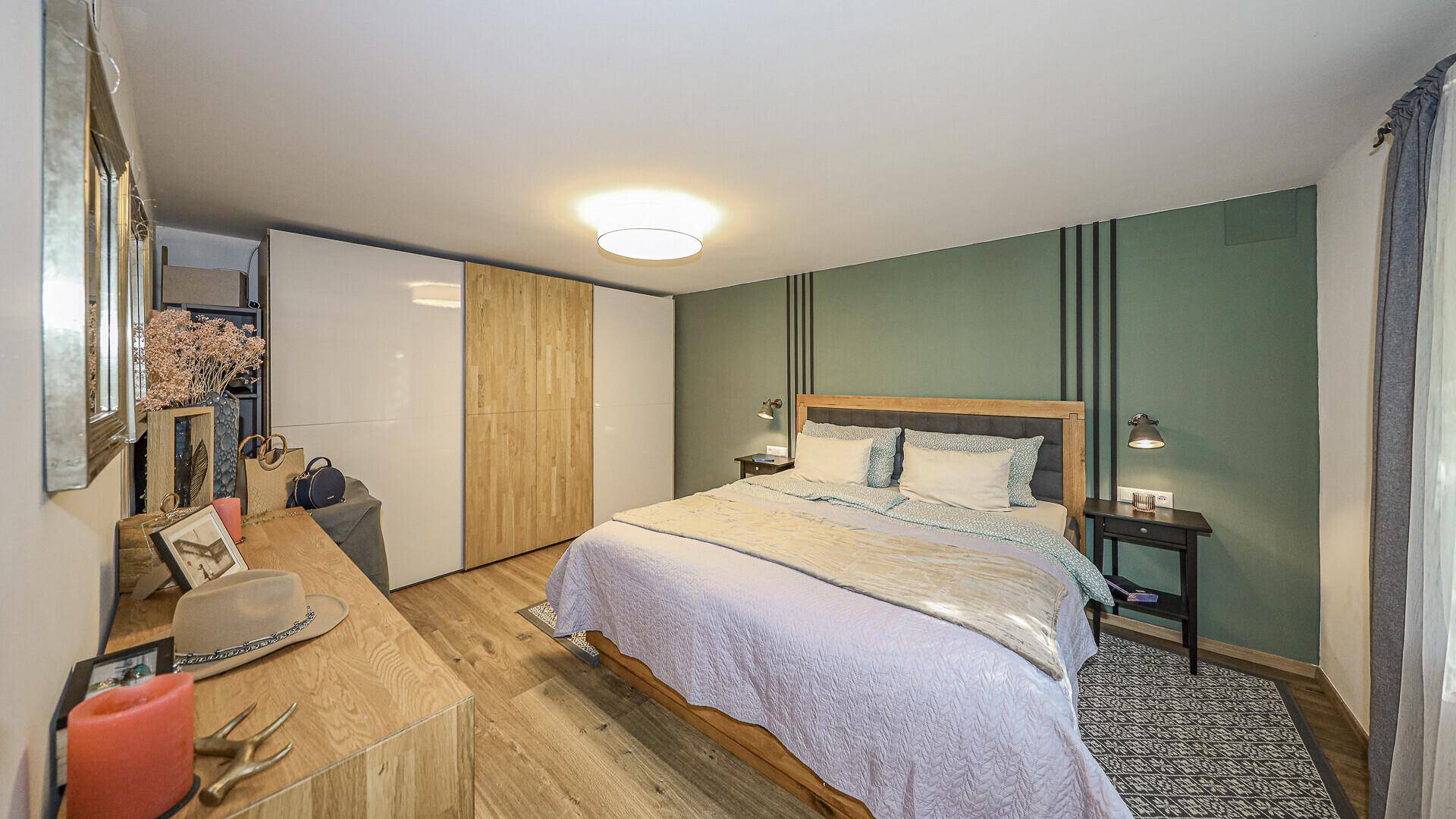 Helles Schlafzimmer mit Holzboden, grüner Akzentwand und modernen Einbauschränken.