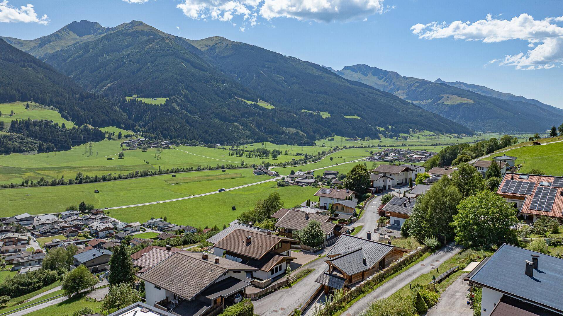 Panoramablick auf die Siedlung in einer weiten grünen Tal- und Berglandschaft.