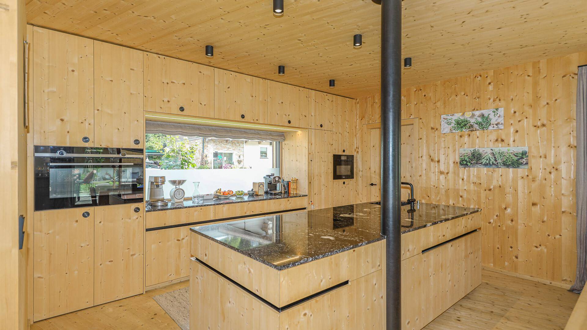 Voll ausgestattete Holzküche mit modernen Einbaugeräten und Fenster mit Blick ins Grüne.