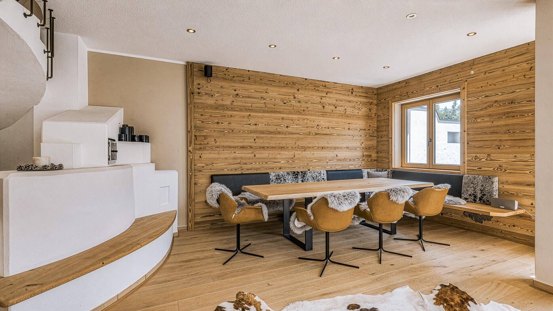 Rustikaler Essbereich mit Holztisch, Eckbank und traditionellem Kachelofen-ähnlichem Design.