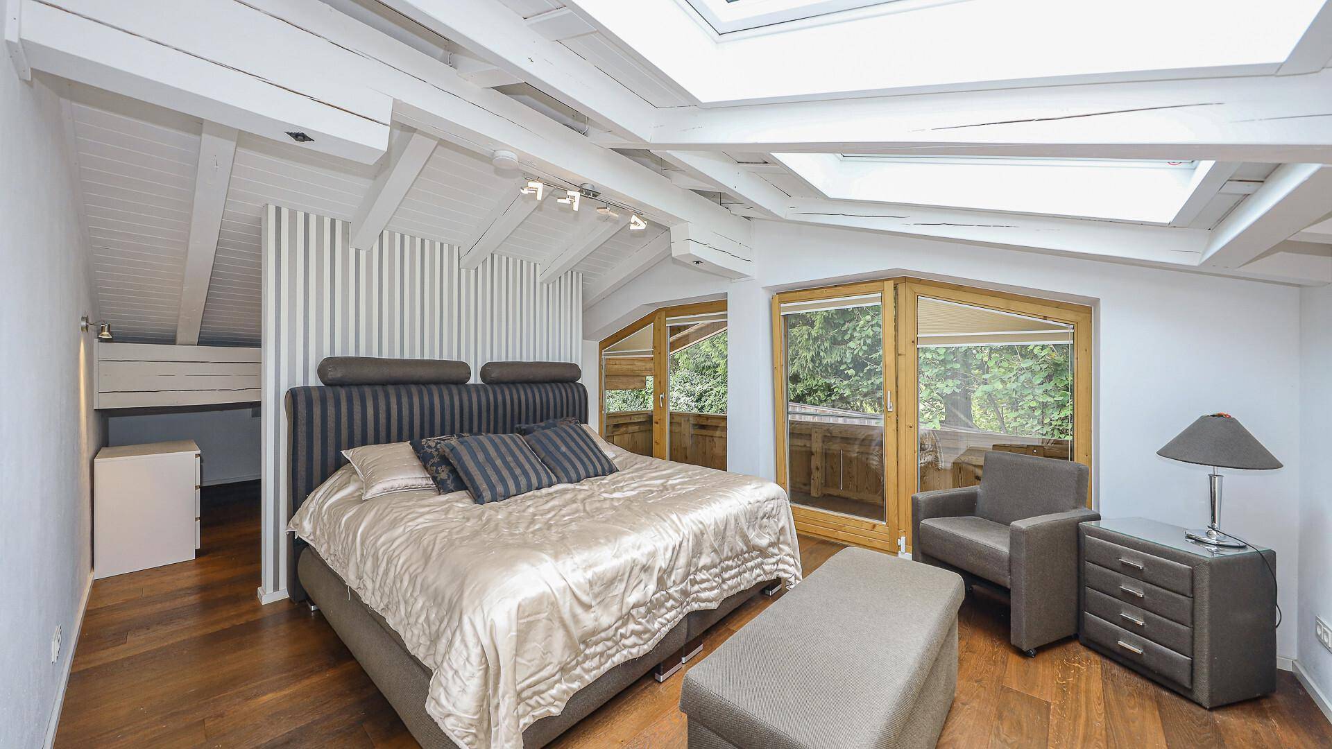 Helles Schlafzimmer im Dachgeschoss mit Holzbalken, großen Dachfenstern und Balkonzugang.