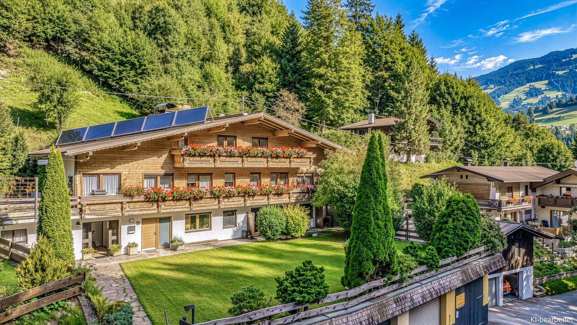 Traditionelles Holzchalet mit blühenden Balkonen, großem Rasen und Solaranlage, eingebettet in die grüne Berglandschaft.