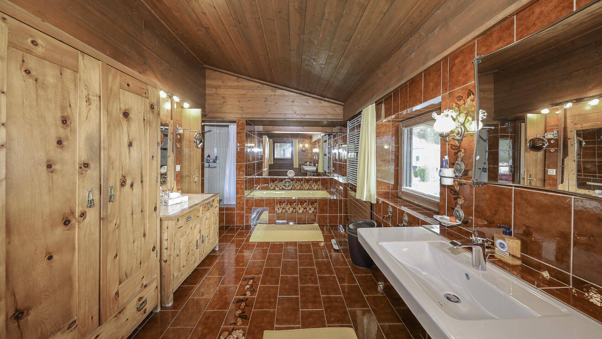 Rustikales Badezimmer mit braunen Fliesen, Holzverkleidung und Badewanne.