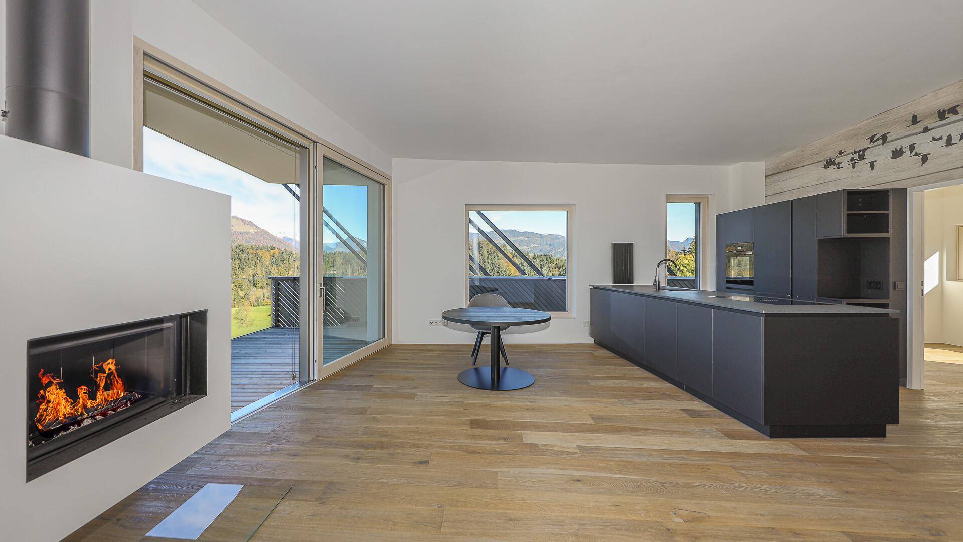 Offene Küche mit Kamin und Essbereich, mit Zugang zur Terrasse und Bergblick.