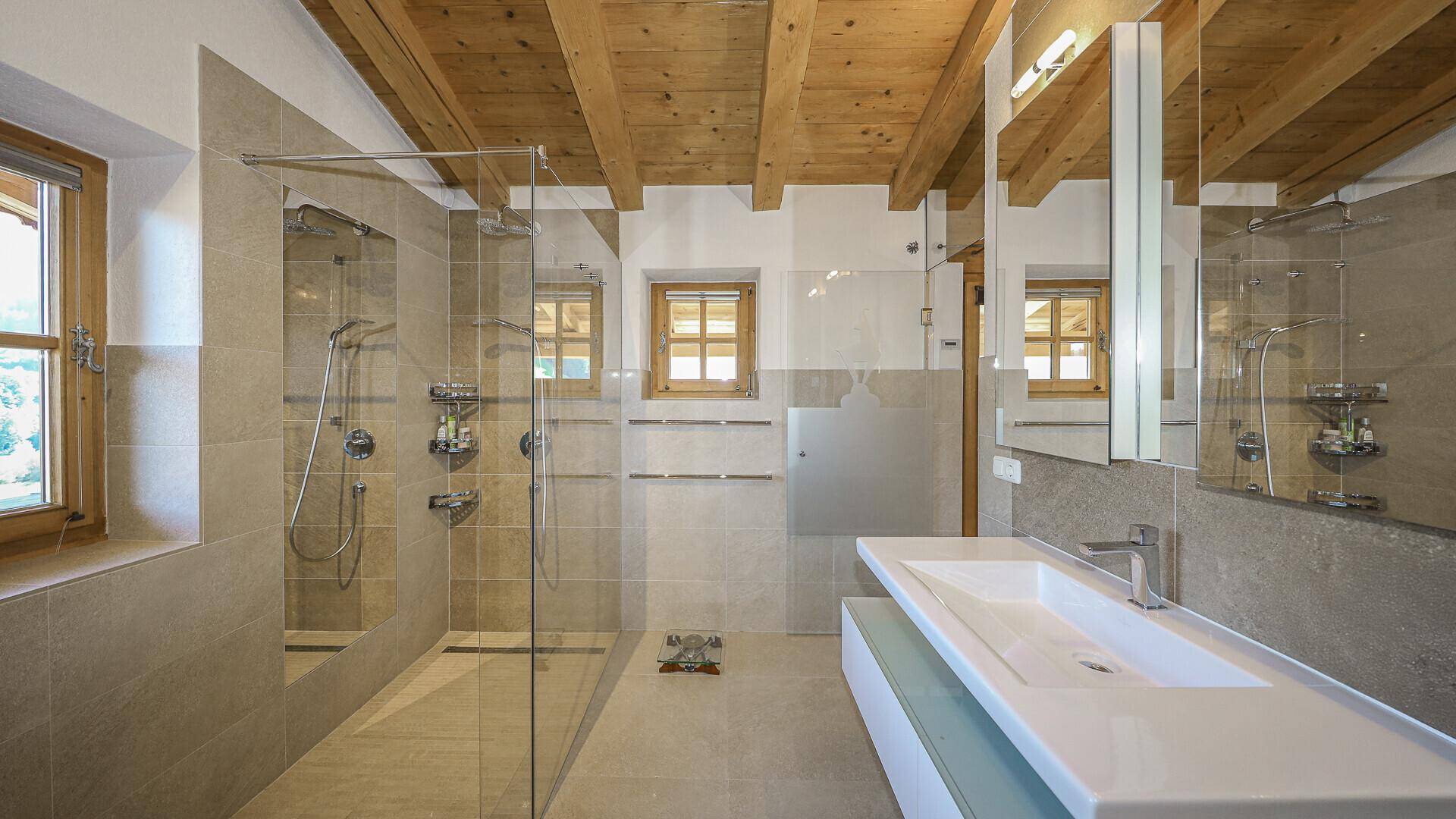 Modernes Badezimmer mit begehbarer Dusche, Doppelwaschbecken und Holzbalkendecke.