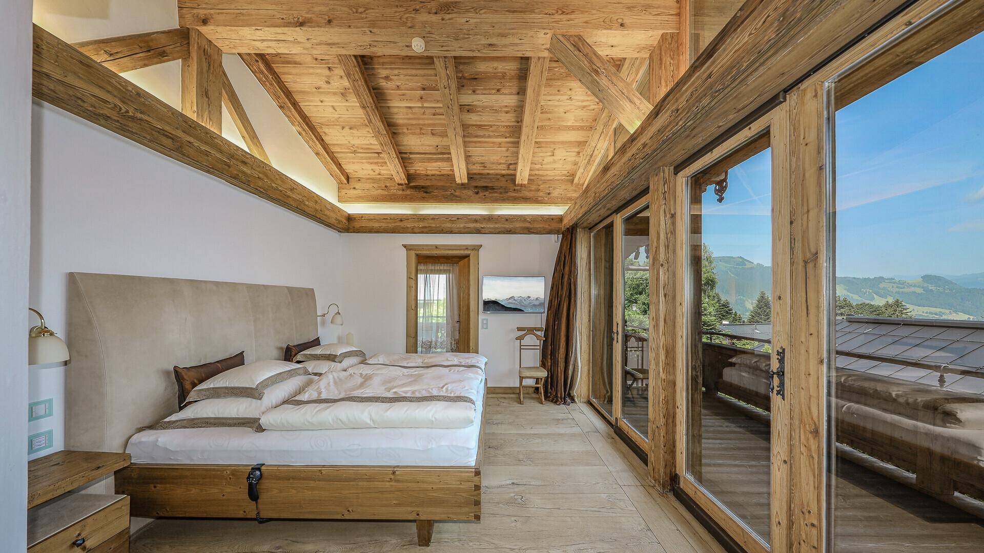 Helles Schlafzimmer mit Holzbalkendecke, Balkonzugang und Panoramablick auf die Berge.