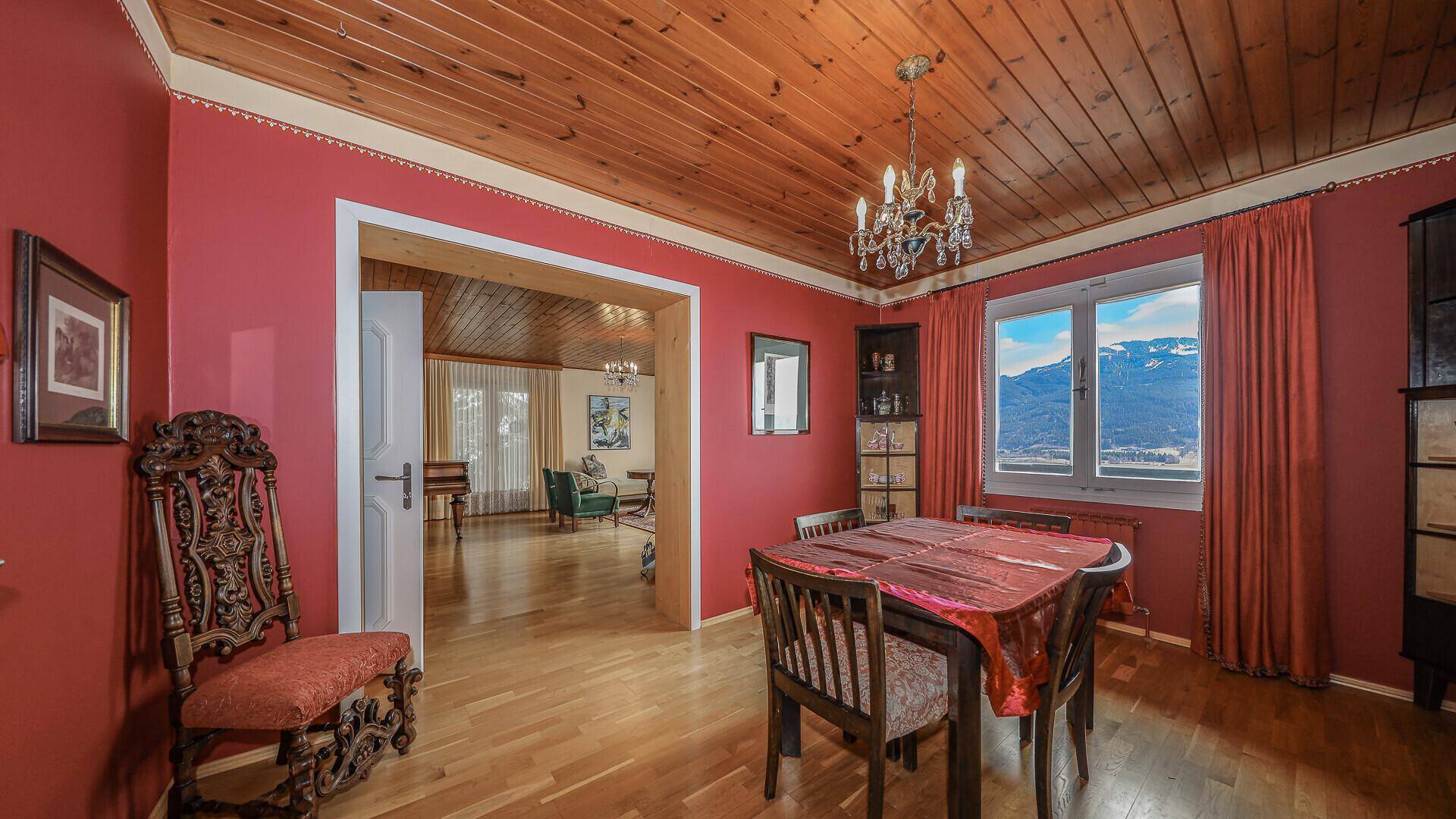 Esszimmer mit roter Wandfarbe, Holzdecke und Parkettboden, bietet einen weiten Bergblick.