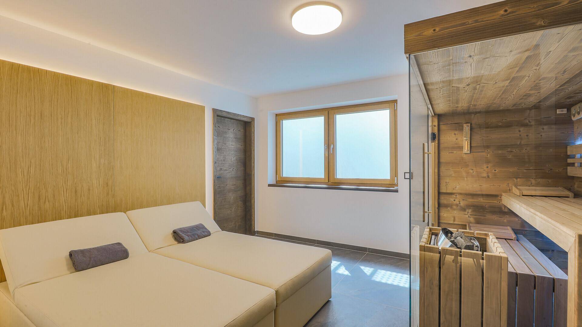 Entspannungsbereich mit Liegen, Fenster und einer modernen Sauna für Wellness-Momente.