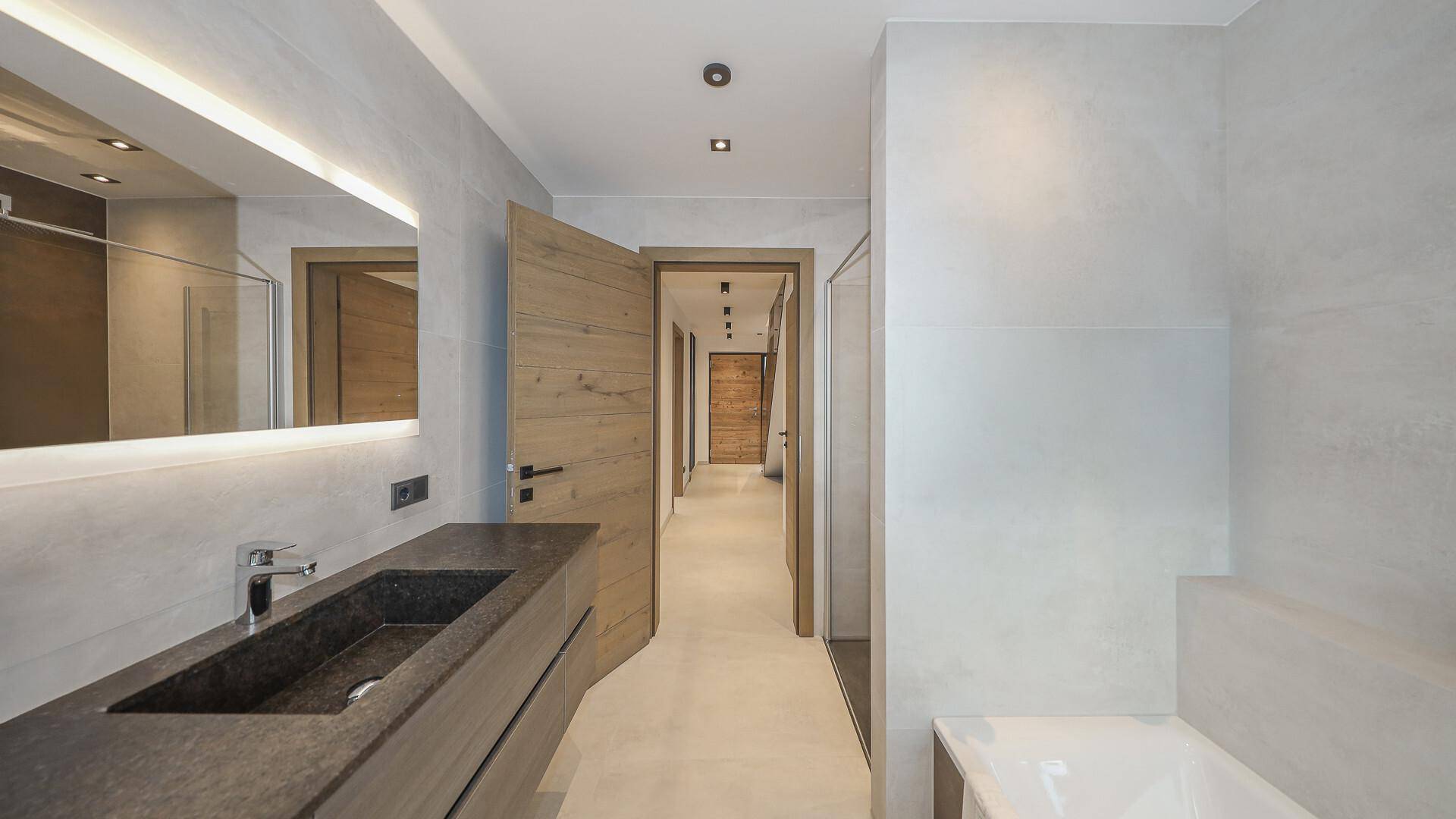 Elegantes Badezimmer mit modernem Waschbecken, beleuchtetem Spiegel und Zugang zum Flur.