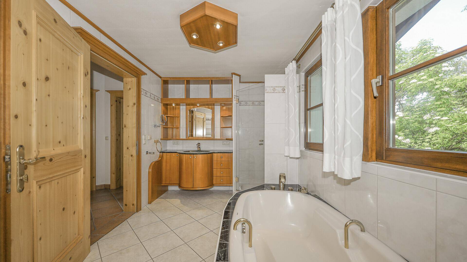 Geräumiges Badezimmer mit Badewanne, Dusche, Holzwaschtisch und Fenster mit Blick ins Grüne.