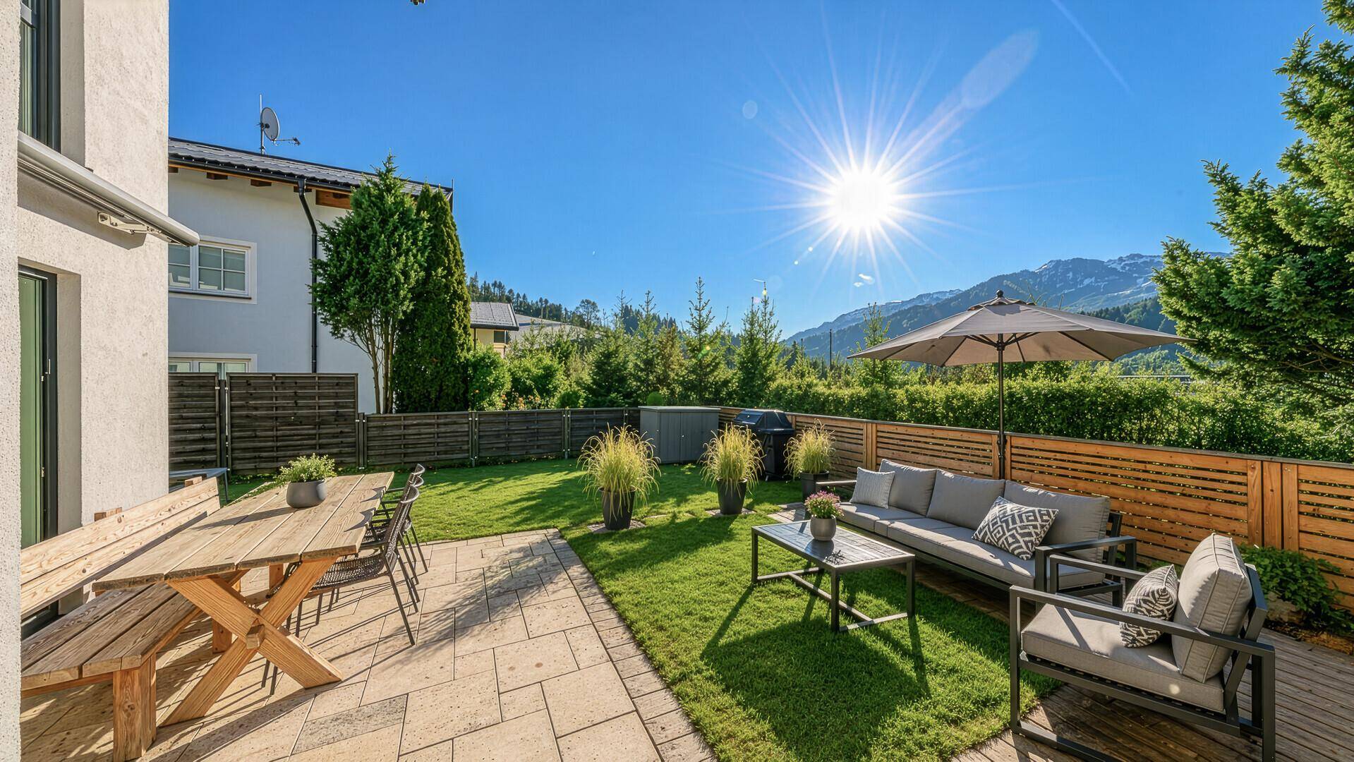 Sonniger Garten mit großer Terrasse, Essbereich im Freien und Liegeflächen, umgeben von grüner Natur.
