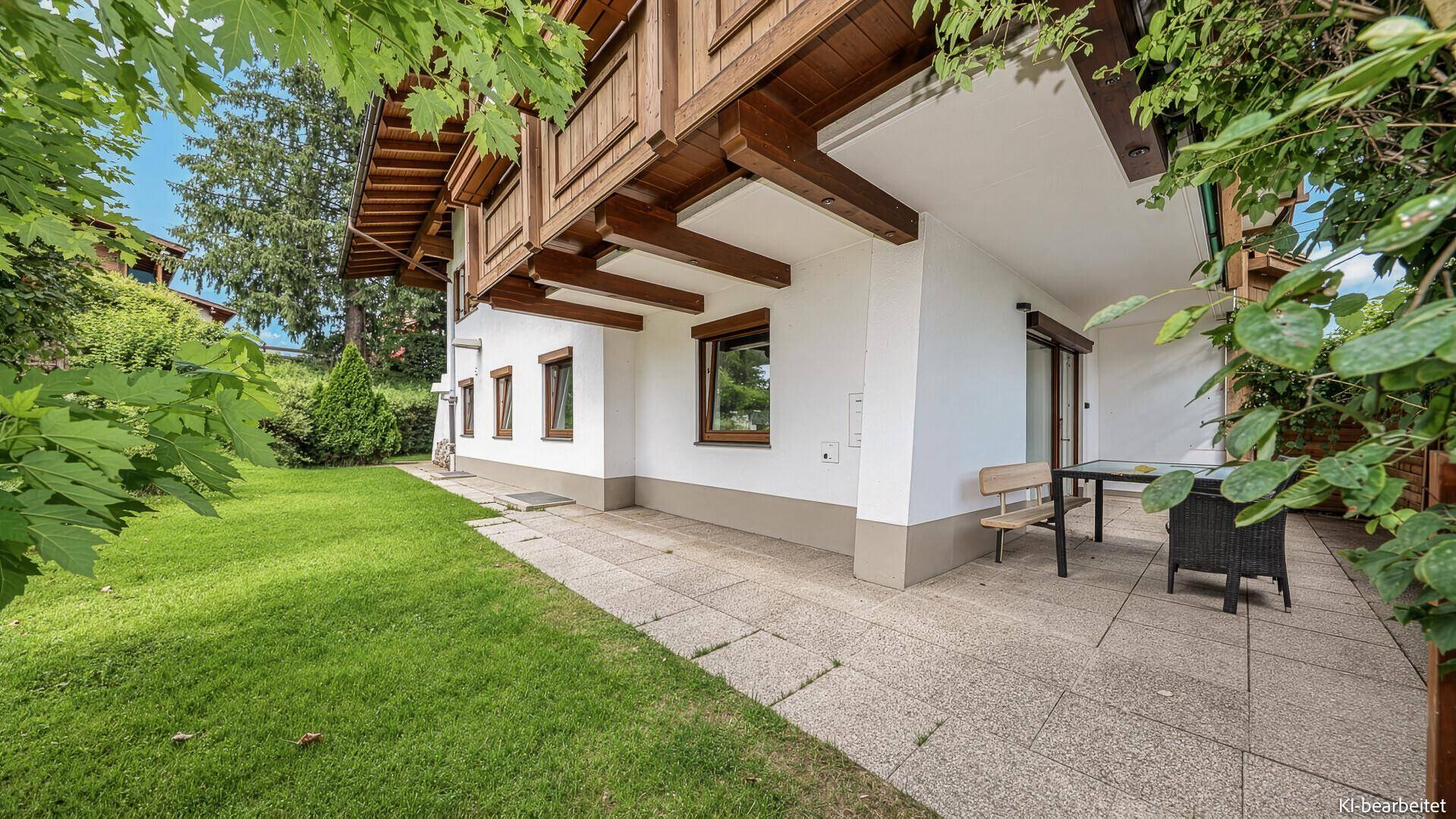 Außenbereich des Hauses mit gepflasterter Terrasse und weitläufiger Rasenfläche, umgeben von Bäumen.