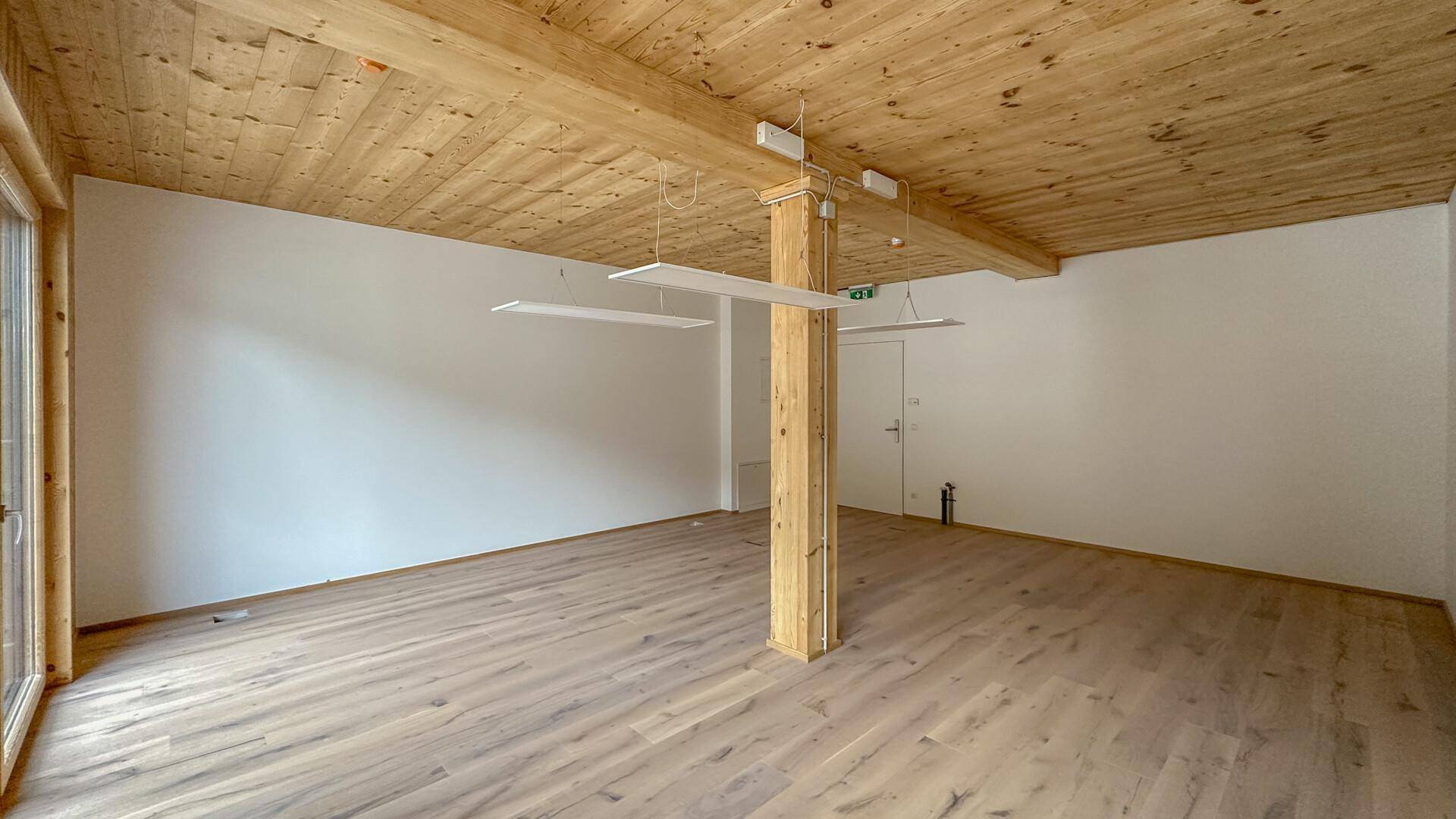 Geräumiger, leerer Raum mit Holzboden, Holzbalken und einer Mischung aus Holz- und hellen Wänden.