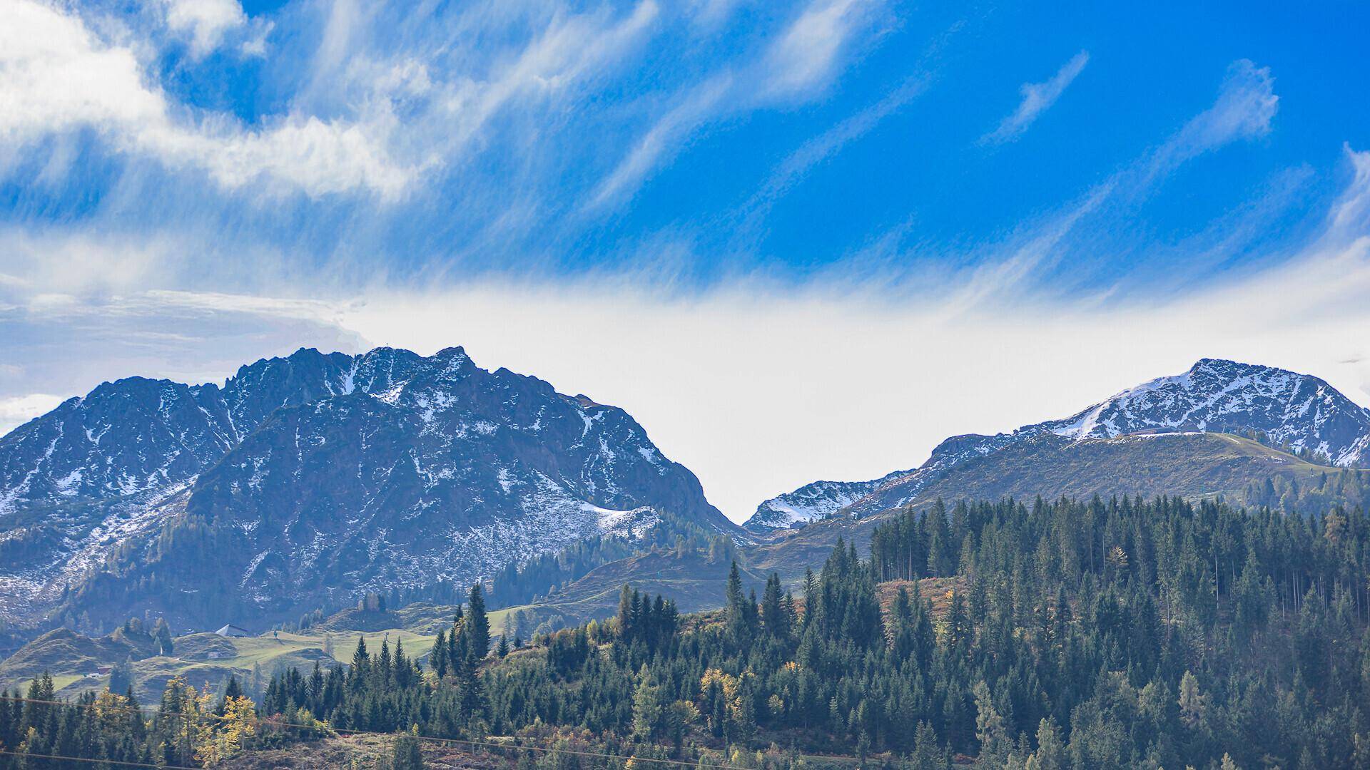 Weite Landschaft mit bewaldeten Bergen und einem strahlend blauen Himmel mit Wolkenformationen.