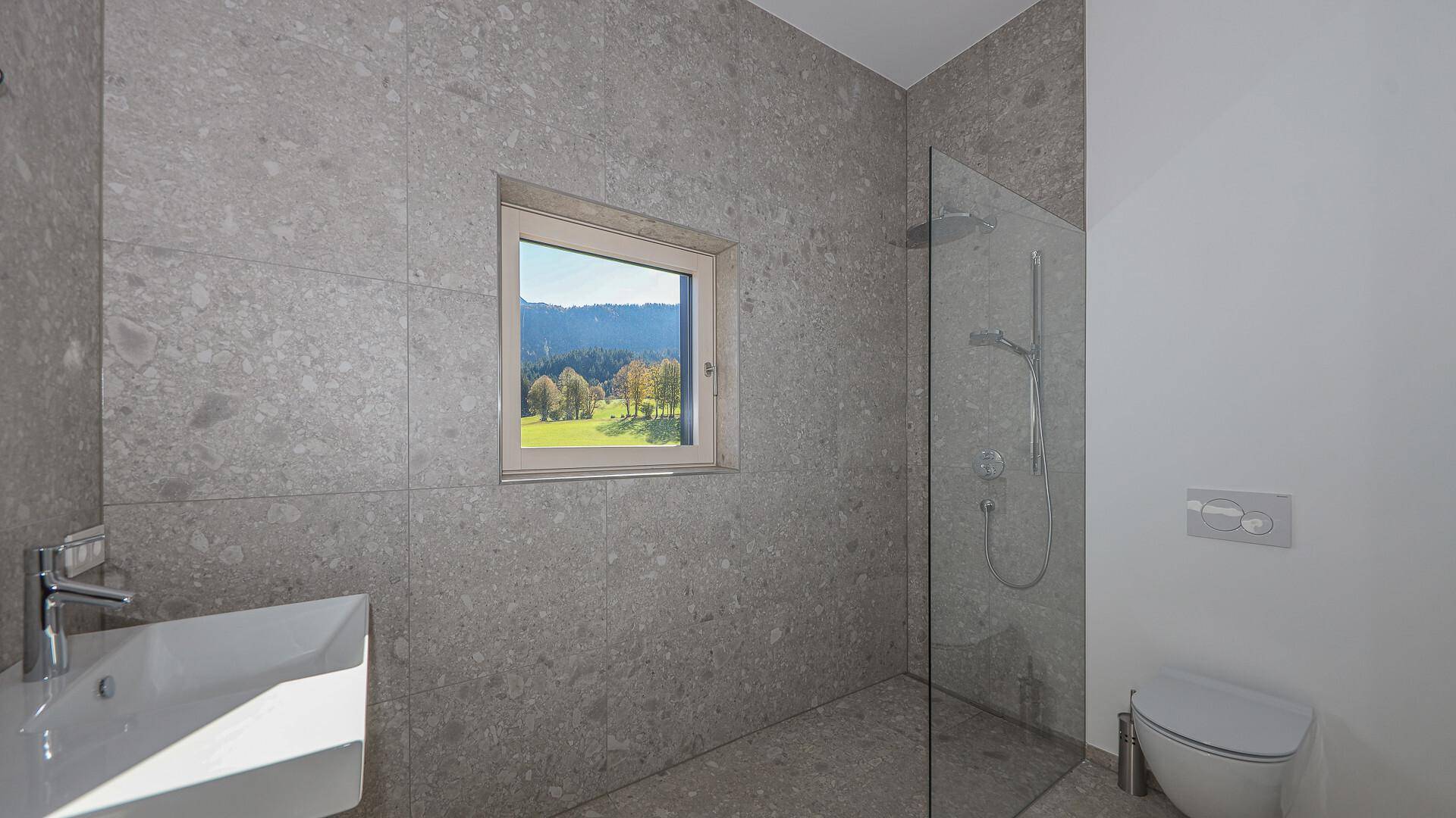 Modernes Badezimmer mit grauen Fliesen, ebenerdiger Dusche und Fenster mit Bergblick.